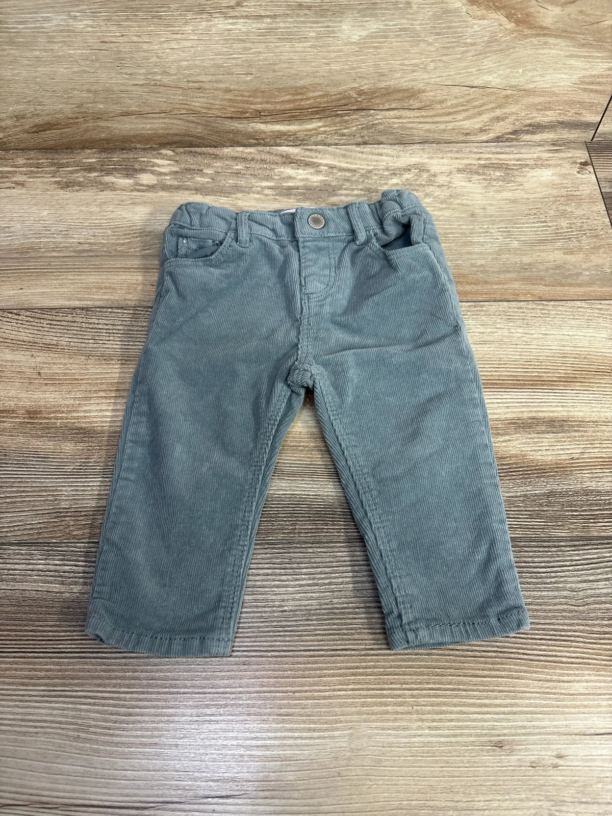Flat-lay of Zara light blue corduroy baby pants showing front pockets, button closure, and belt loops on wooden background