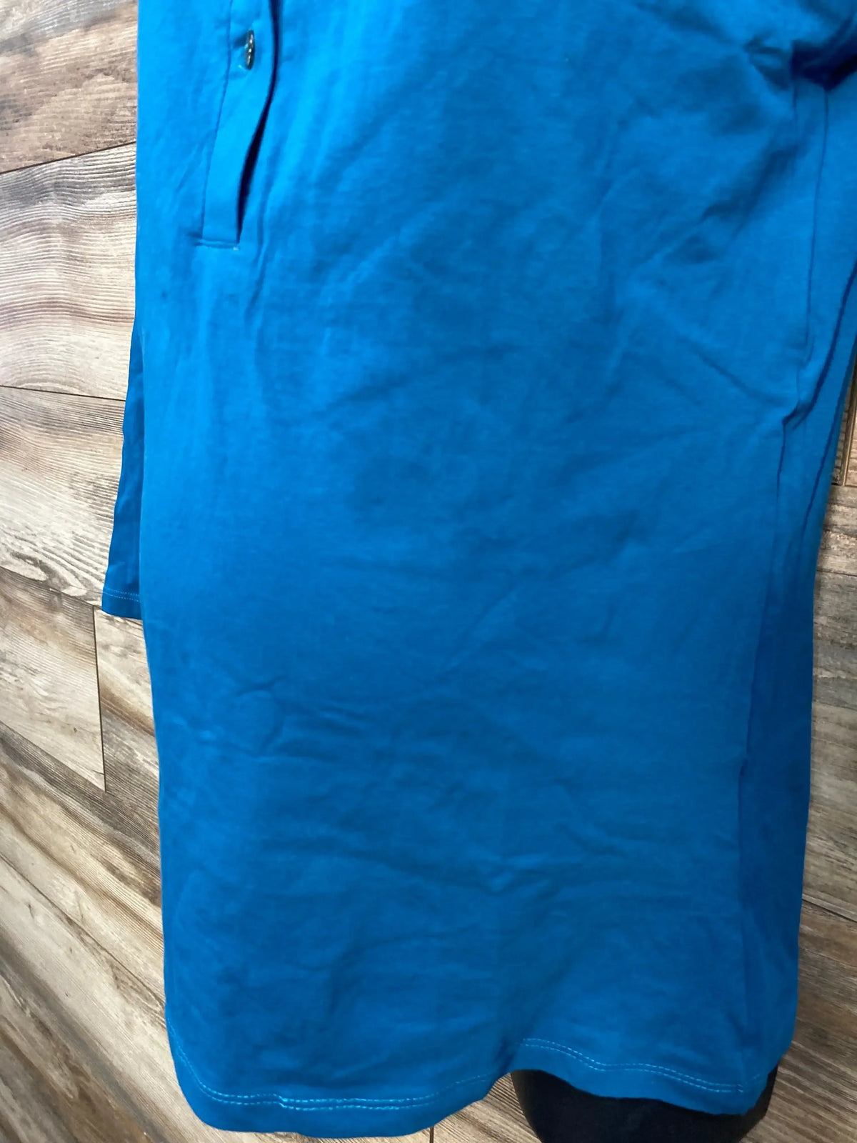 Front close-up of blue maternity nursing Henley shirt showing button placket, pocket detail and hem against wood plank background