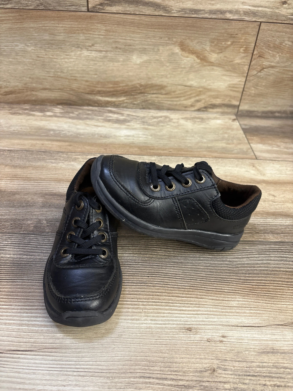 Front and side view of black uniform Oxford shoes with lace-up closure on a wood-look floor