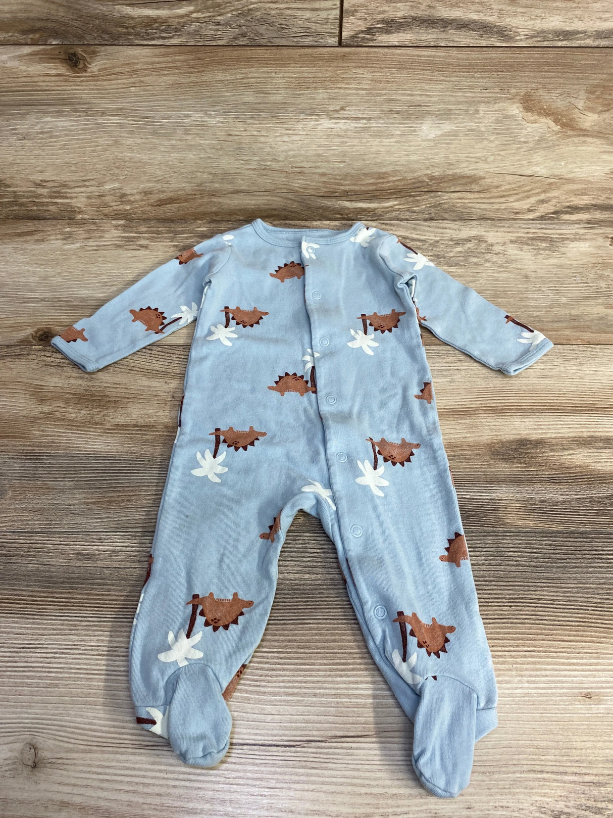 Flat-lay of blue Carter's 6M footed sleeper showing brown dinosaur print and front snap closure on wood plank background