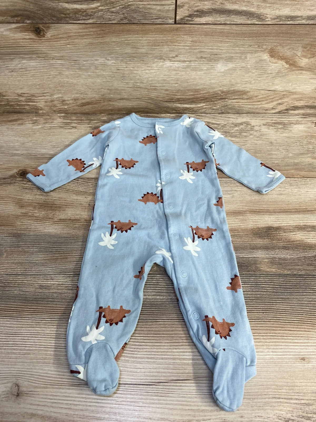 Flat-lay of blue Carter's 6M footed sleeper showing brown dinosaur print and front snap closure on wood plank background