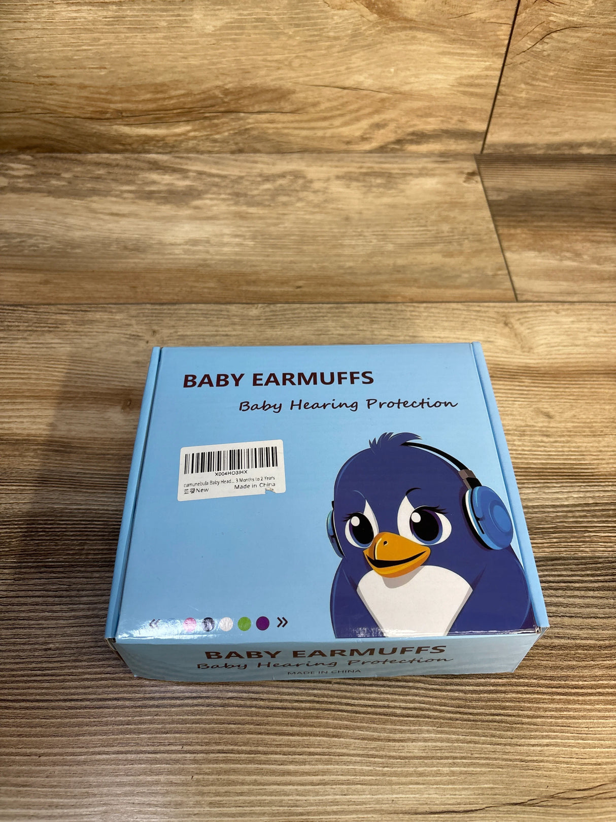 Top view of blue 2-in-1 baby earmuffs box with penguin illustration and ‘Baby Earmuffs Baby Hearing Protection’ text on wood