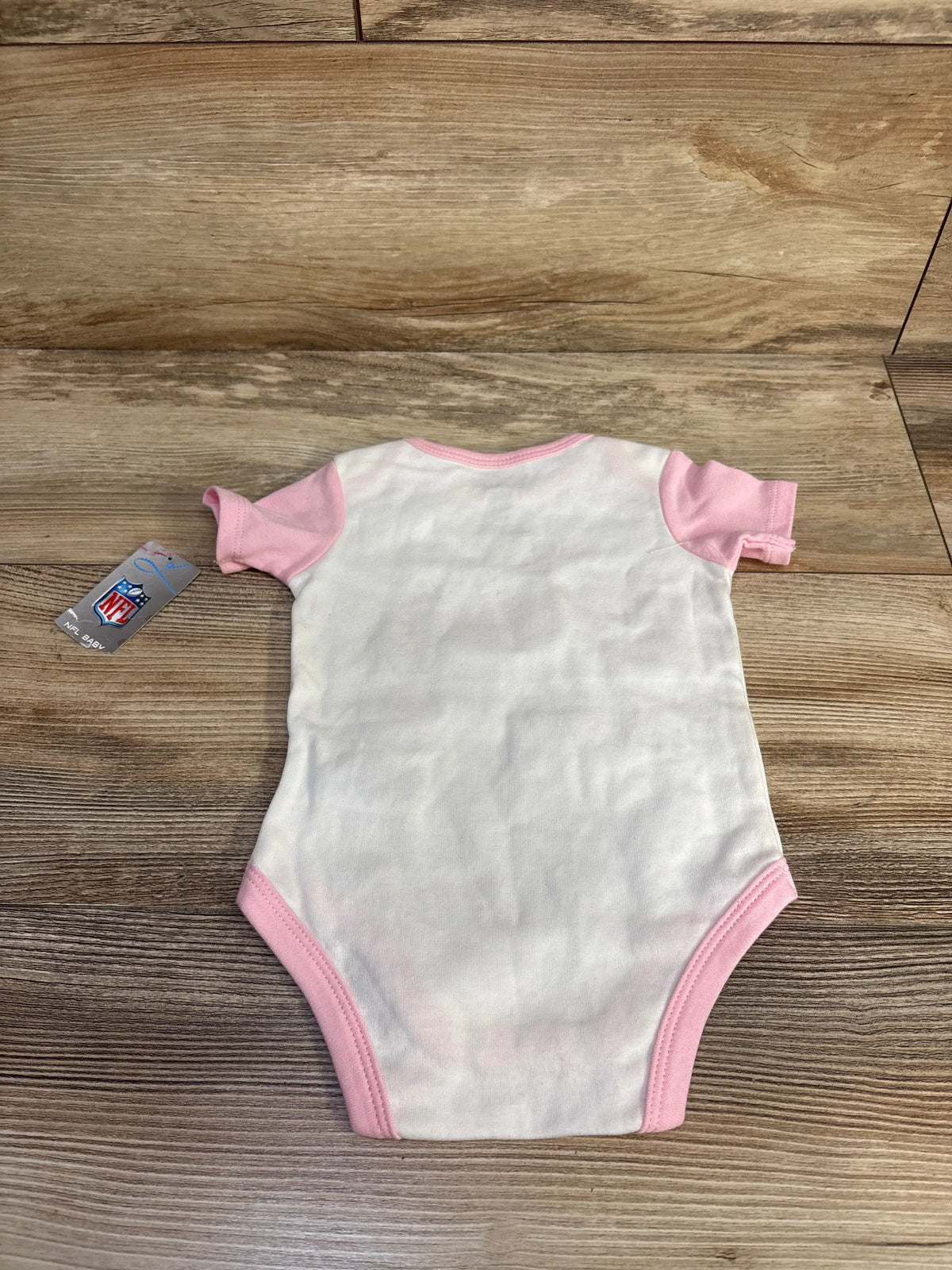 Back view of white NFL baby bodysuit showcasing pink trim and short sleeves on a wood grain background