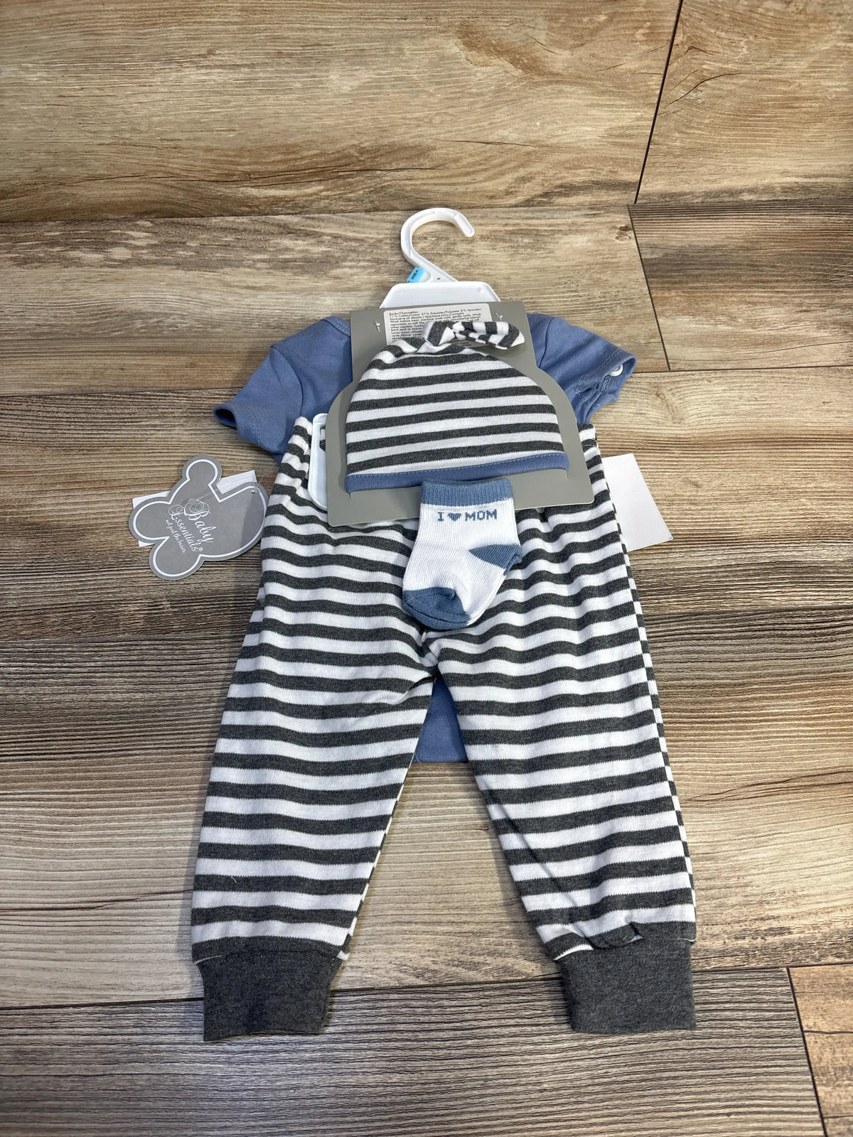 Top view of Baby Essentials four piece baby boy set showcasing blue bodysuit, striped pants, hat, and socks on wood floor