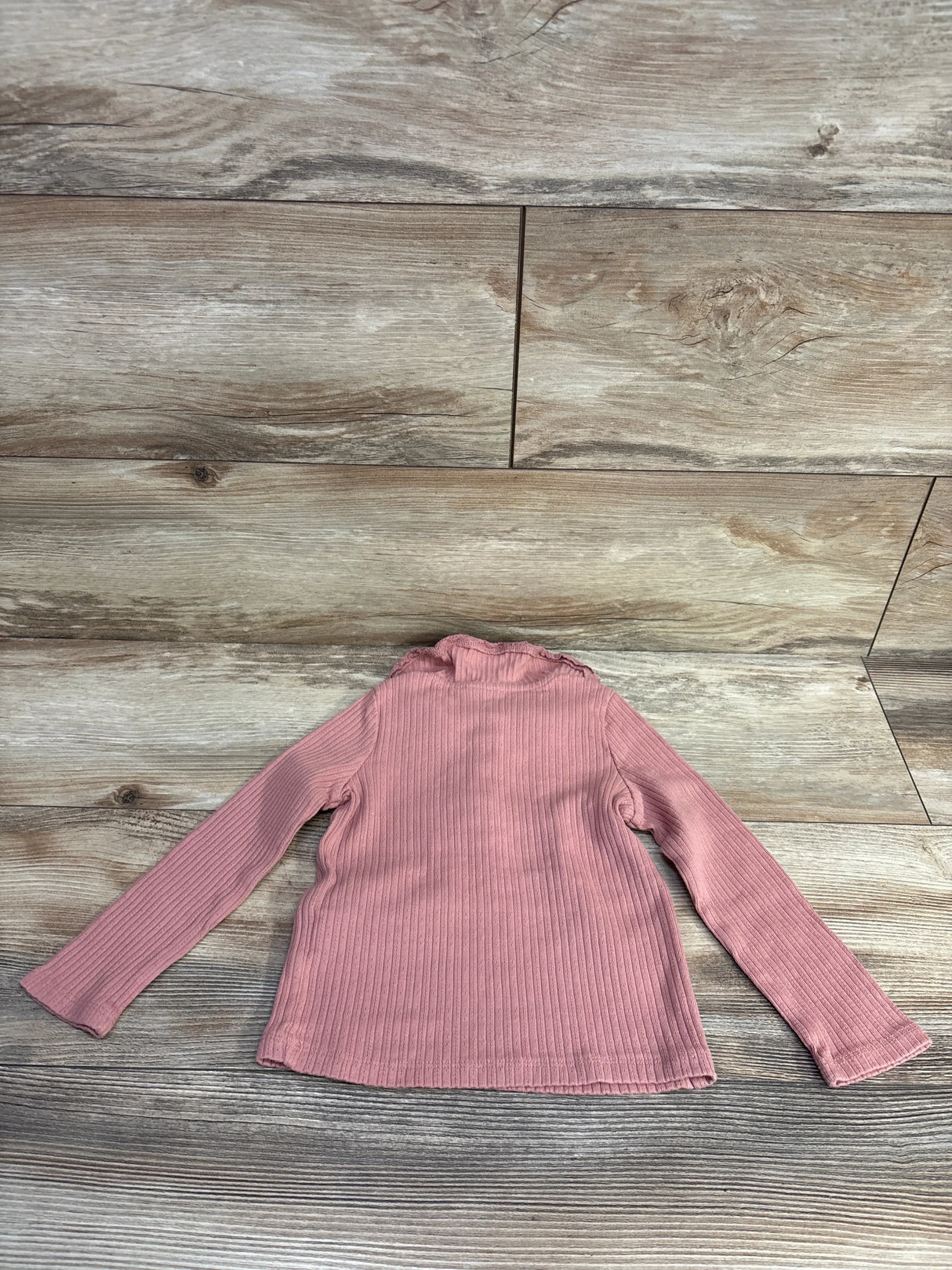 Pink ribbed long sleeve toddler sweater on wooden floor background