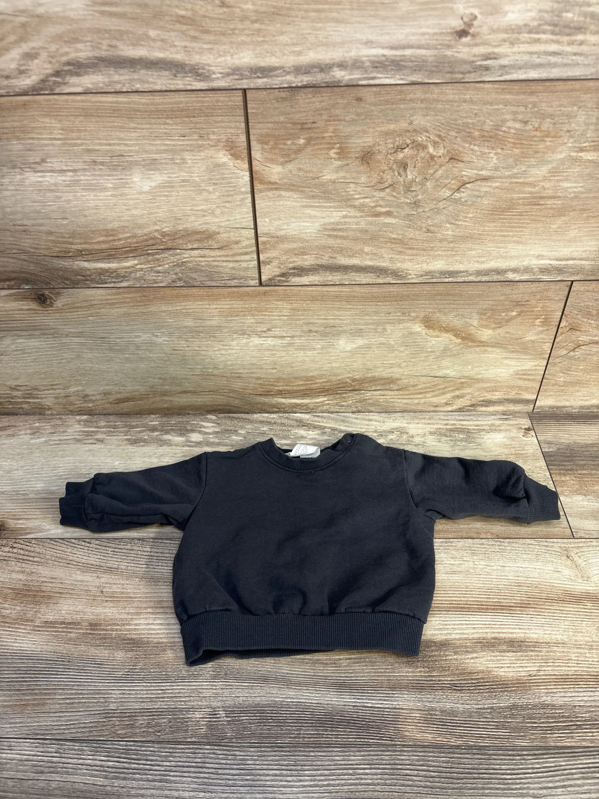 Front view of grey H&M baby sweatshirt in size 3 months showcasing long sleeves, crew neck, and ribbed trim on wood floor