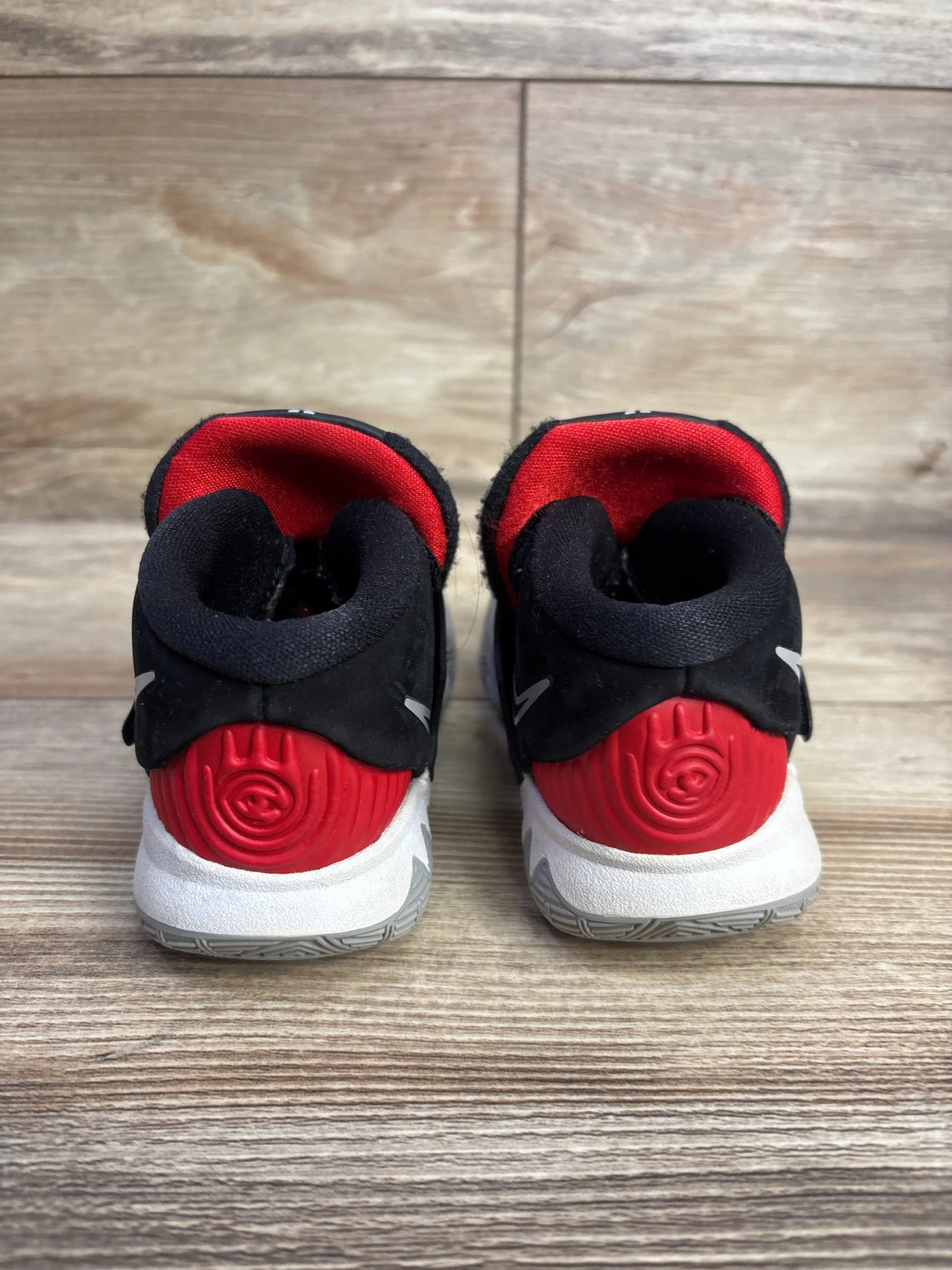Back view of Nike Kyrie 6 TD Bred sneakers showcasing red heel cups, black uppers and white midsoles on wood plank floor