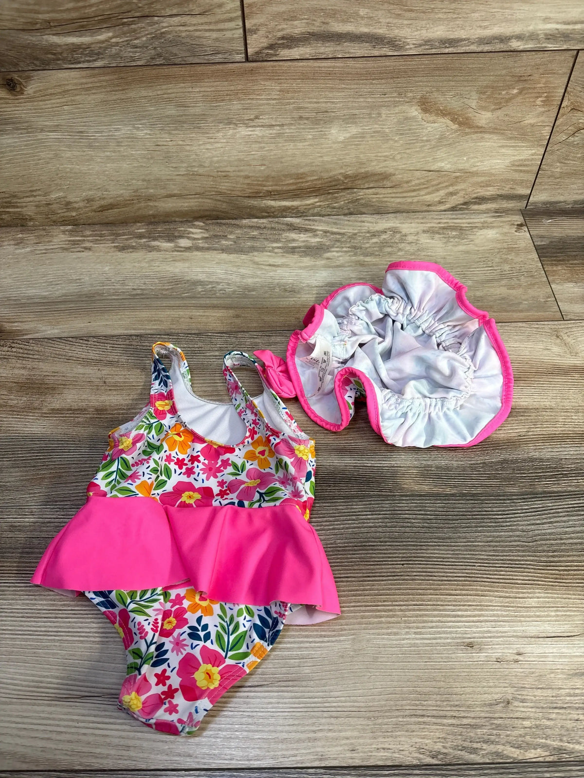 Flat lay of baby floral swimsuit and matching sunhat showcasing pink peplum ruffle on wood floor