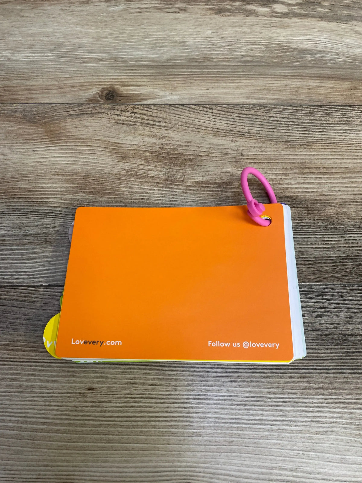 Top-down of Lovevery Persister play guide cards with orange back, pink ring, and visible Lovevery.com text on wood surface