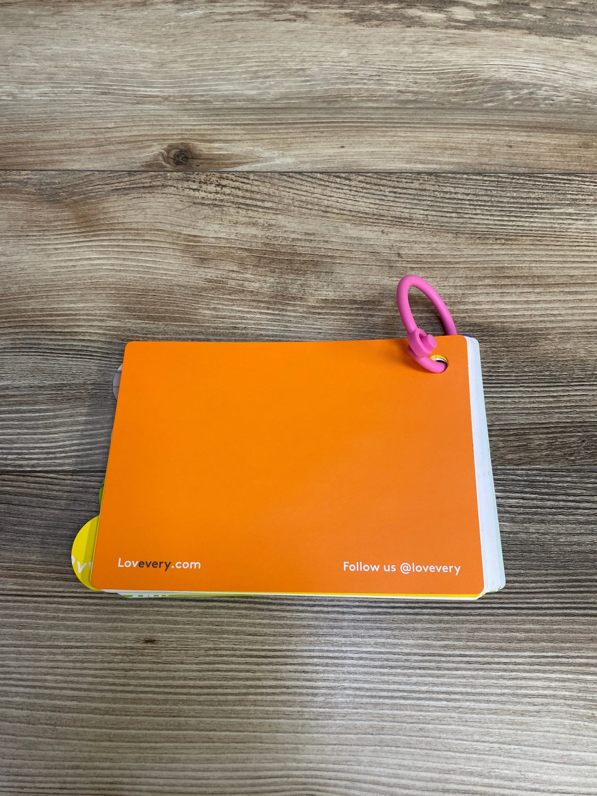 Bright orange flashcard with rounded corners on wooden surface, secured by pink ring, Lovevery branding