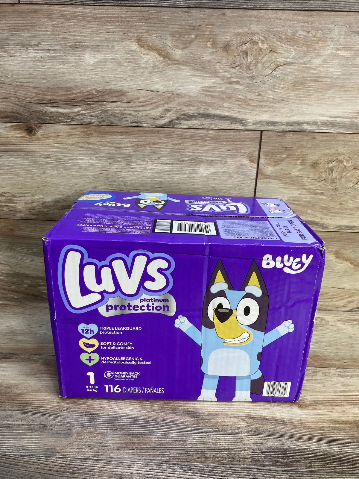 Angled front view of Luvs Bluey size 1 diaper box showing Luvs platinum protection logo and 116-count label on wooden background