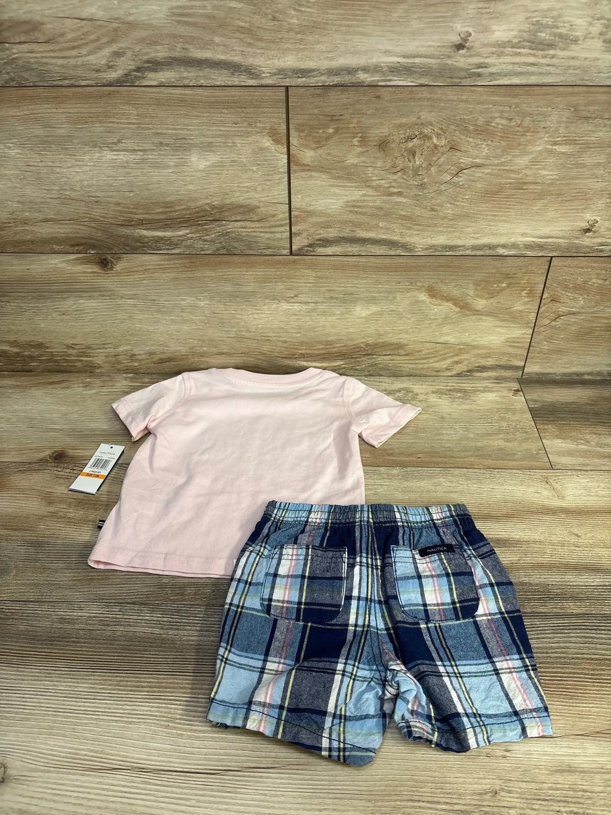 Front view of Nautica two-piece set showcasing pink short-sleeve shirt and blue plaid shorts with drawstring waist and front pockets on wood floor