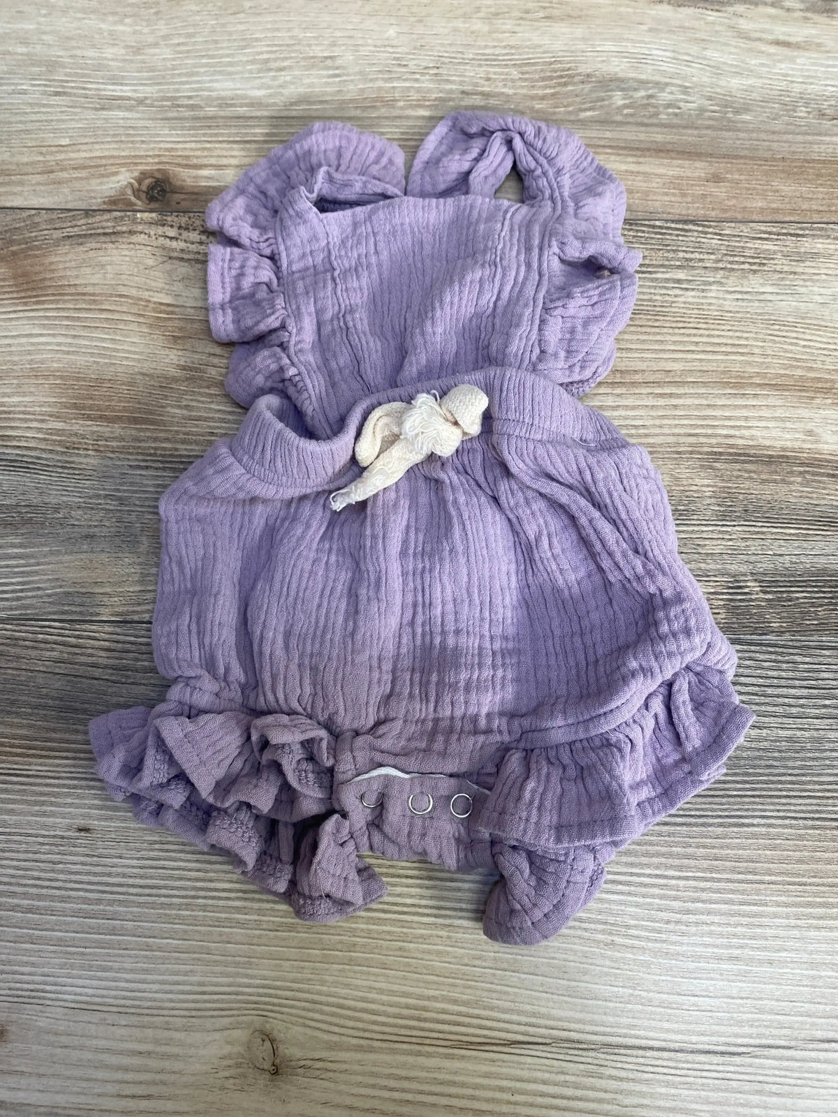 Flat lay of purple baby ruffle romper showcasing crinkled gauze fabric, ruffled straps and snap crotch on wood background