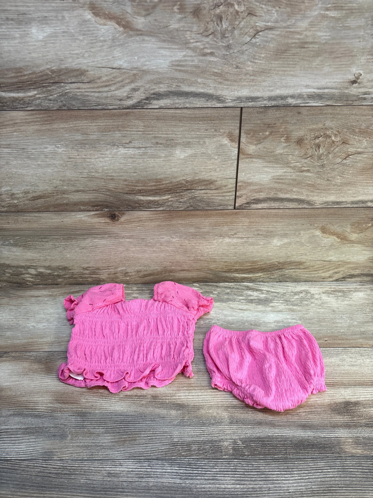 Pink ruffled baby top and bloomers set displayed on wood background