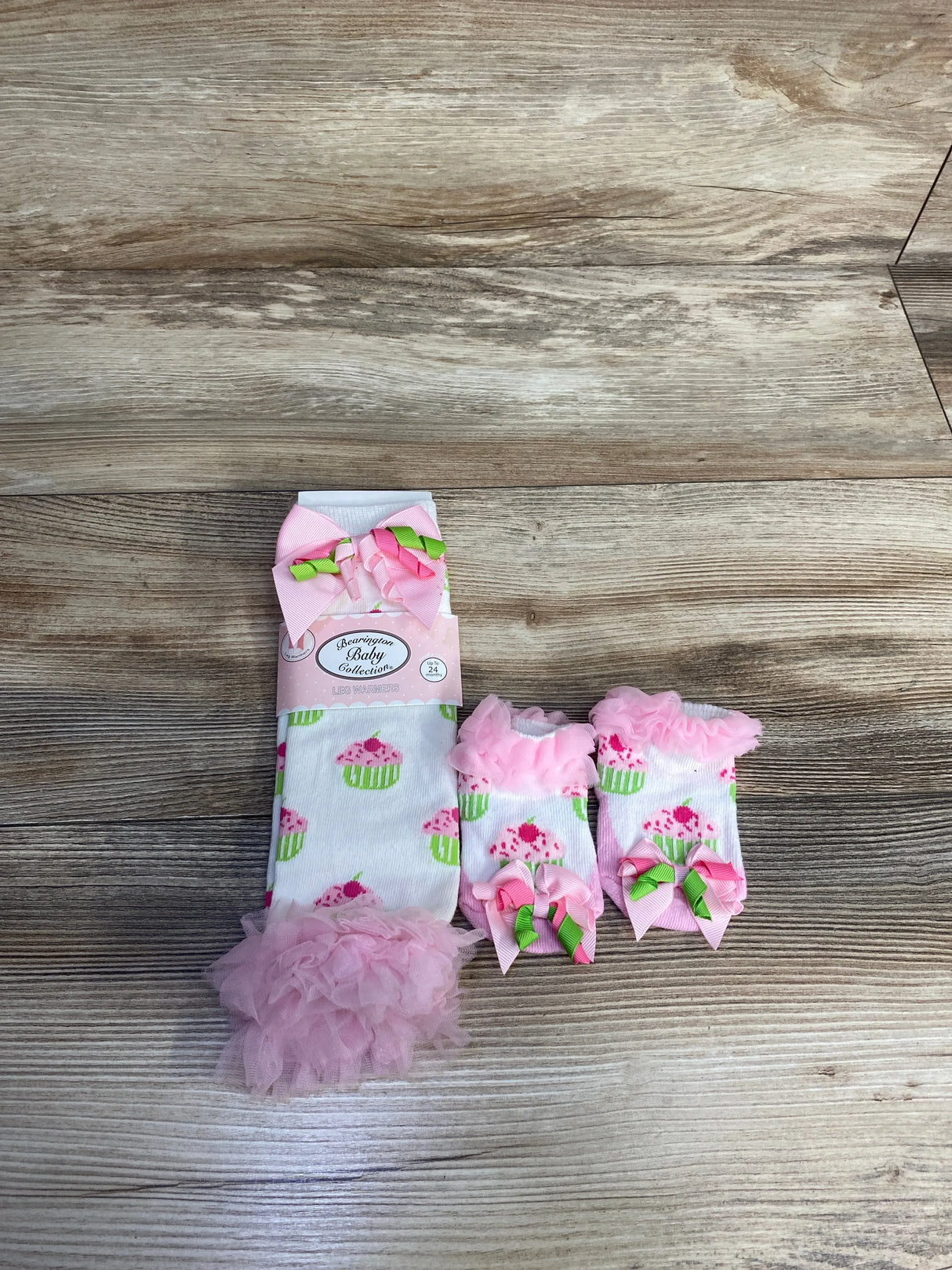 Pink cupcake baby leg warmers and matching socks with bows on wooden surface