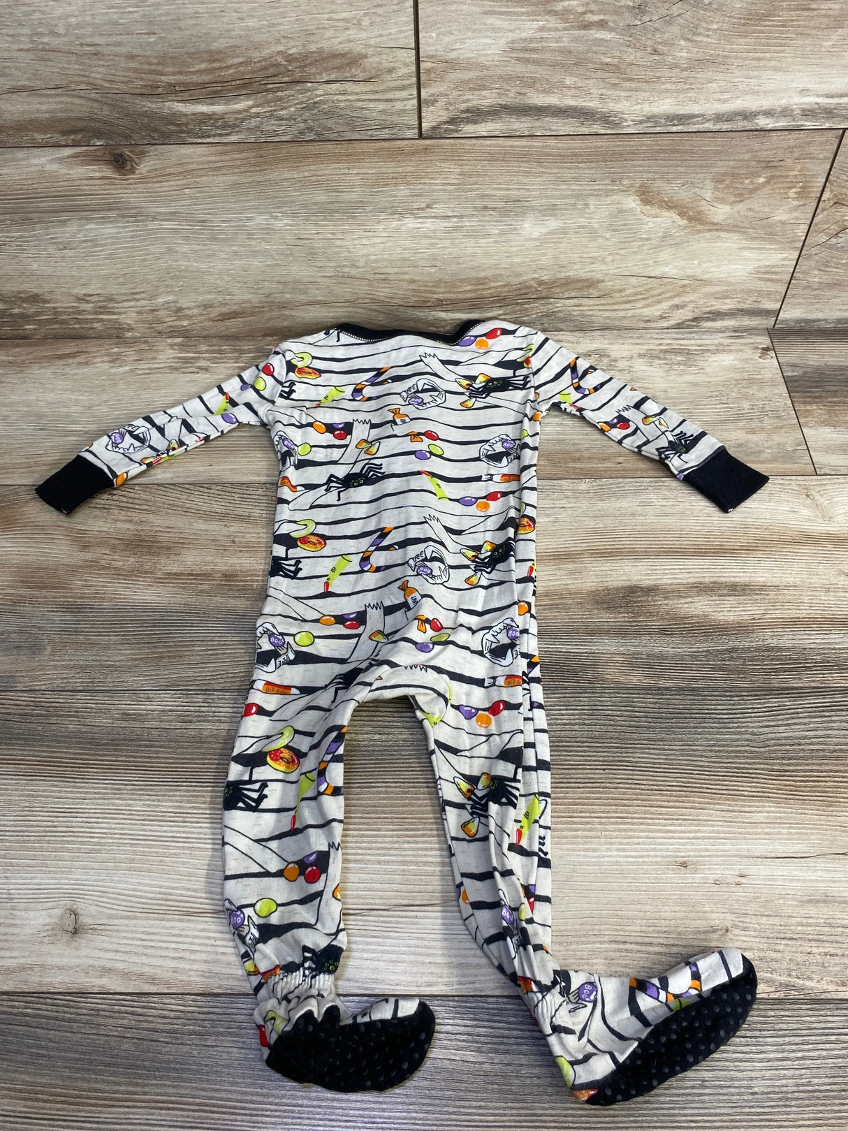 Halloween-themed baby onesie with candy and spider print, long sleeves, footed design on wood floor