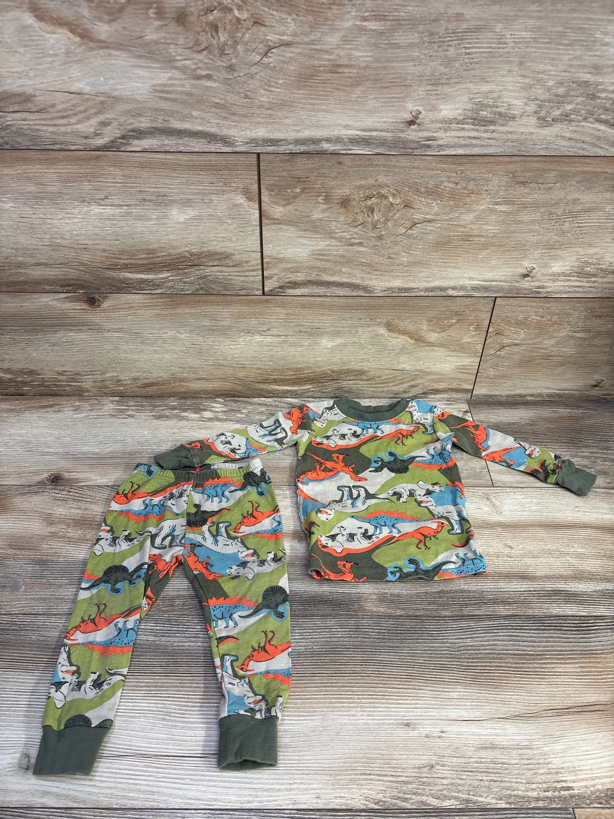 Top-down view of Carter’s two-piece pajamas showcasing a green dinosaur print and ribbed cuffs on a wood floor