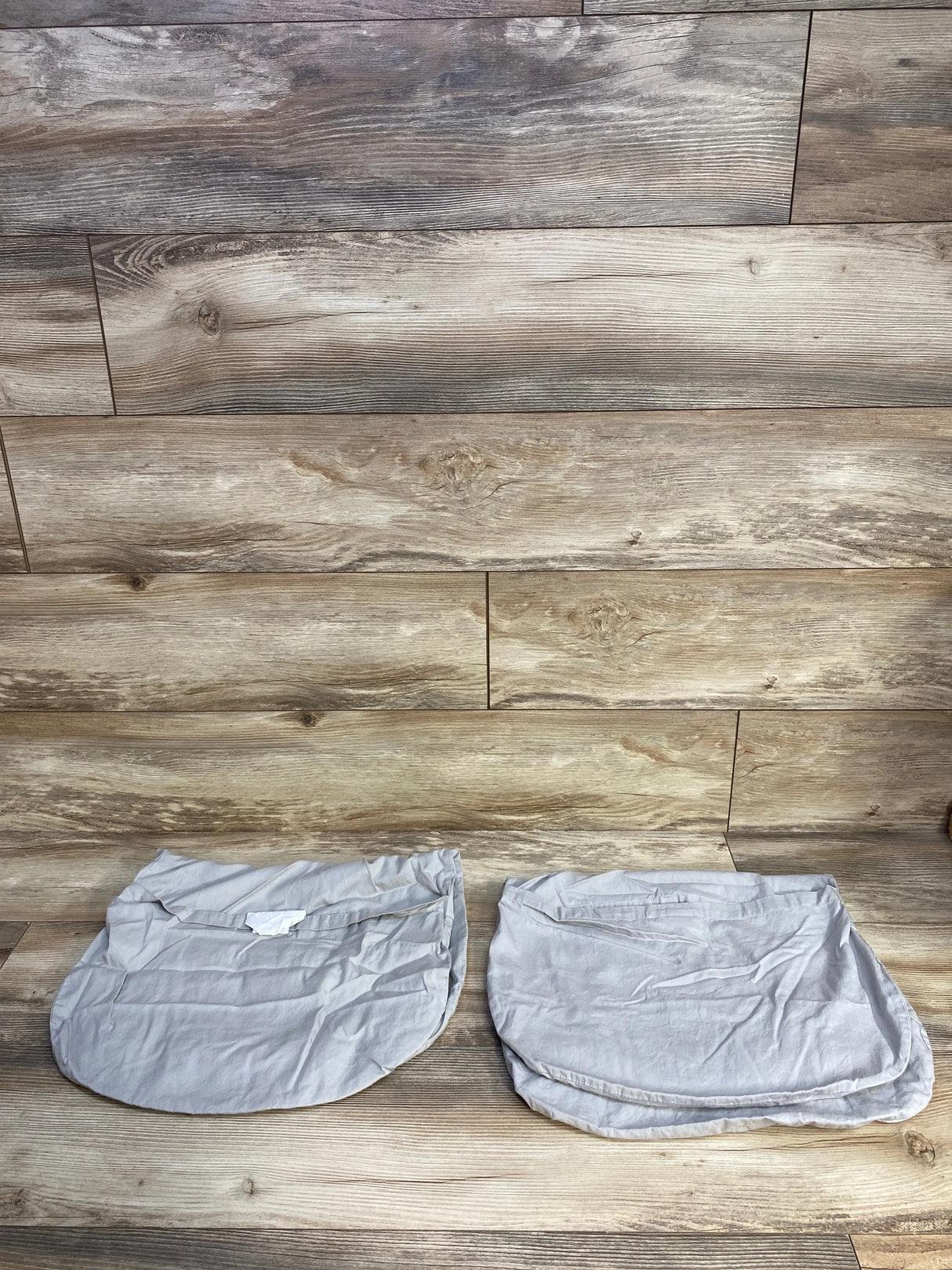 Top view of TILLYOU 2pk Baby Bassinet Sheets, Grey showcasing two fitted oval sheets on a wood plank floor