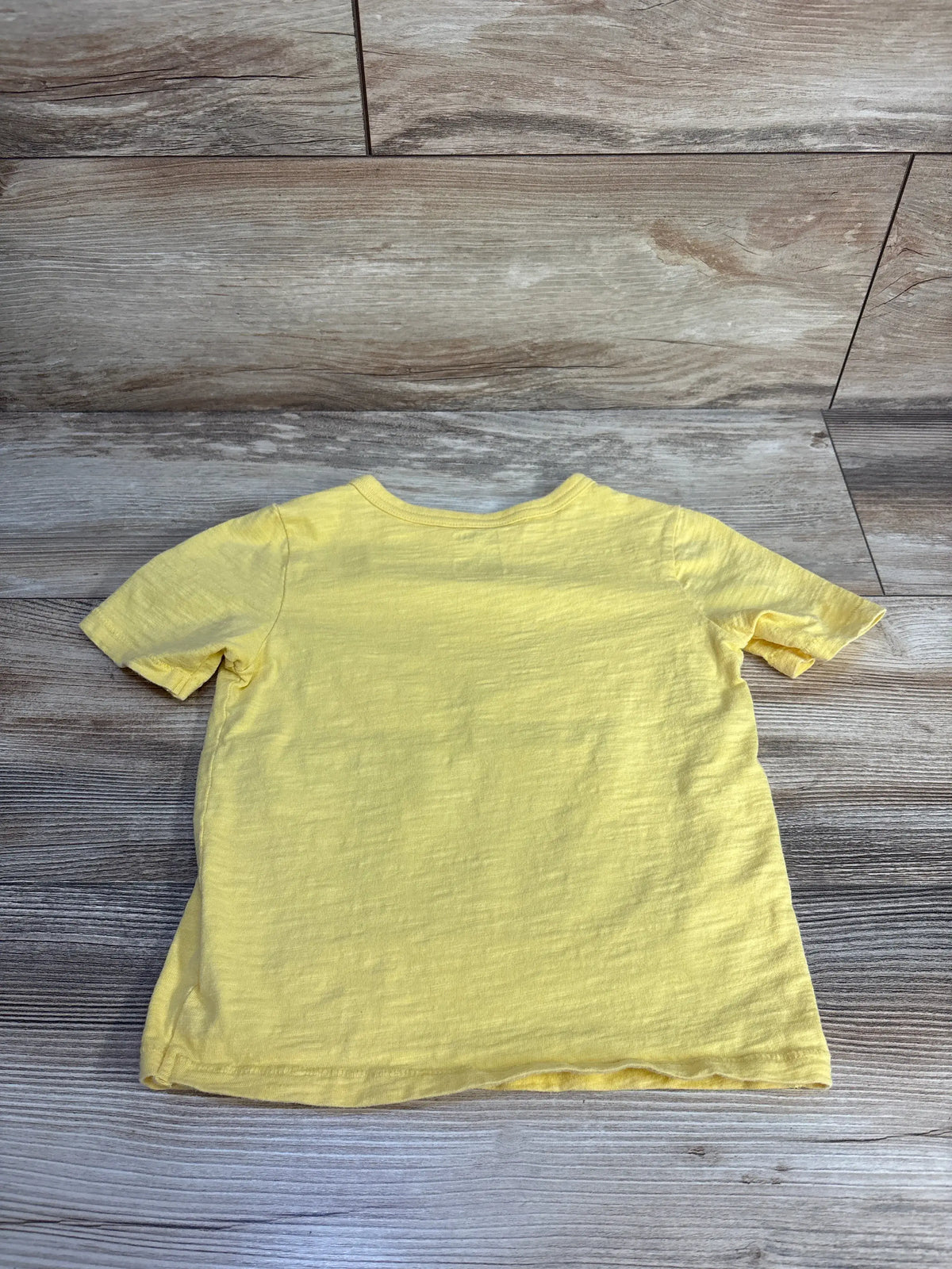 Back view of a yellow Baby Gap toddler t-shirt laid flat on a wooden surface.