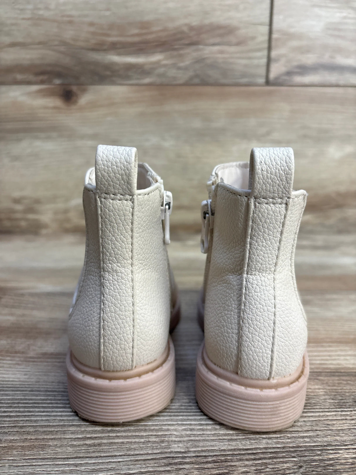 White toddler boots with pink soles, textured leather, and side zippers on wood floor