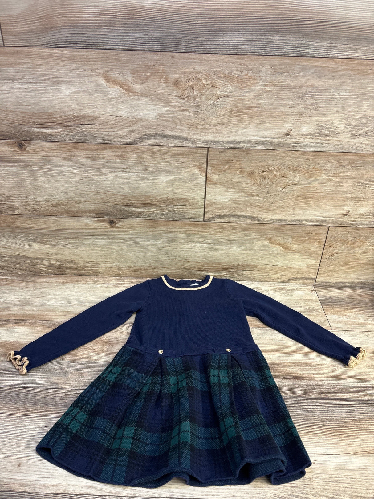 Flat lay of tartan sweater dress with navy bodice, green and navy plaid skirt, ruffle cuffs and gold buttons on floor