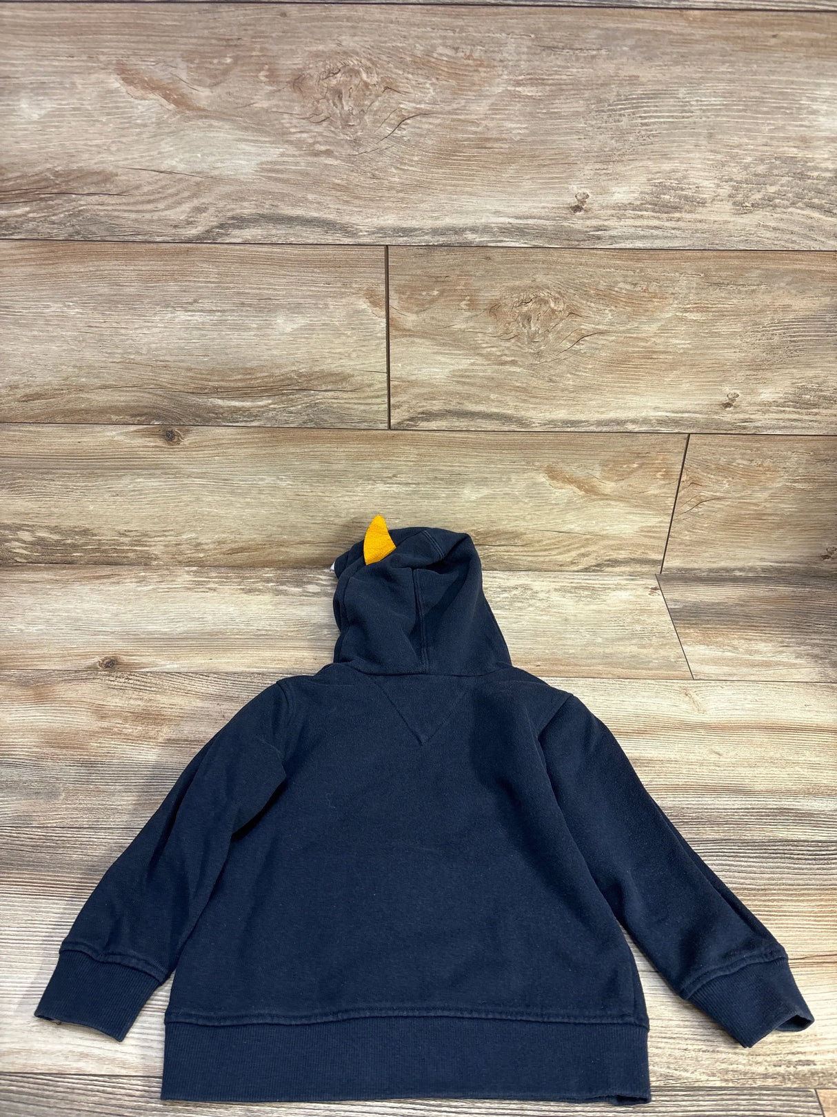 Back view of navy toddler hoodie (size 4T) showing hood with yellow horn detail on light wood plank background