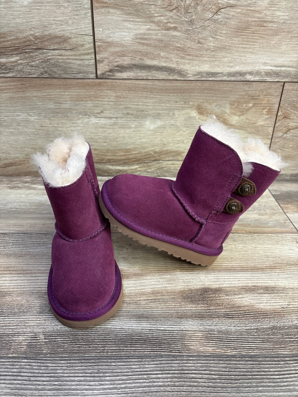 Front and side views of purple UGG Maybin pull on boots showcasing fleece lining and button details on wood flooring