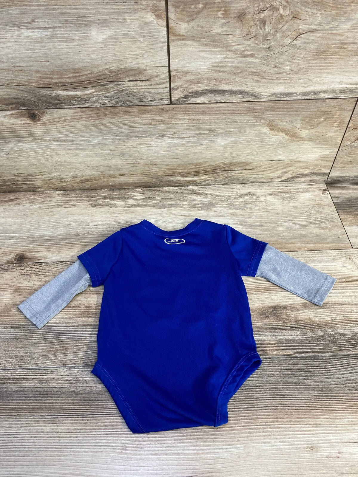 Front view of Under Armour blue bodysuit showcasing gray long sleeves on a wood-look background