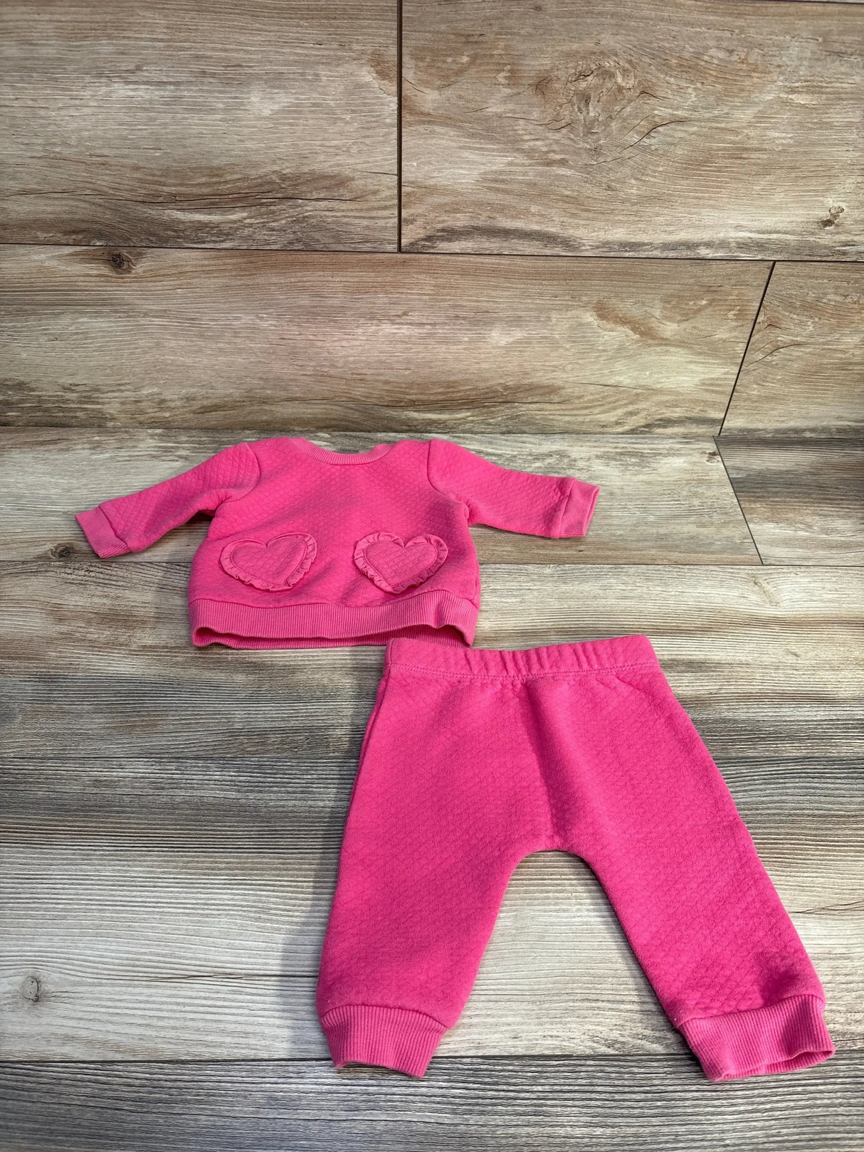 Front view of 2-piece pink quilted sweatshirt and pants (3M) showing ruffled heart pockets and ribbed cuffs on wood background