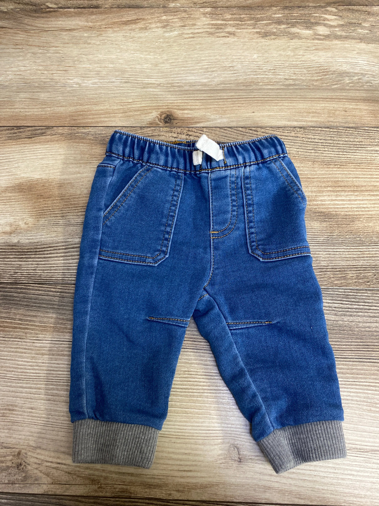 Blue toddler sized jeans with elastic waistband and grey cuffs on wood floor background