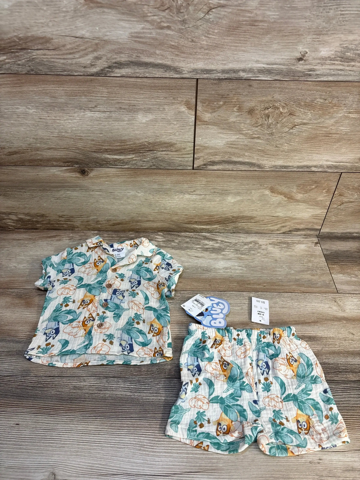 Front view of cream Bluey gauze shirt and shorts set with button-up shirt and character leaf print on wood background