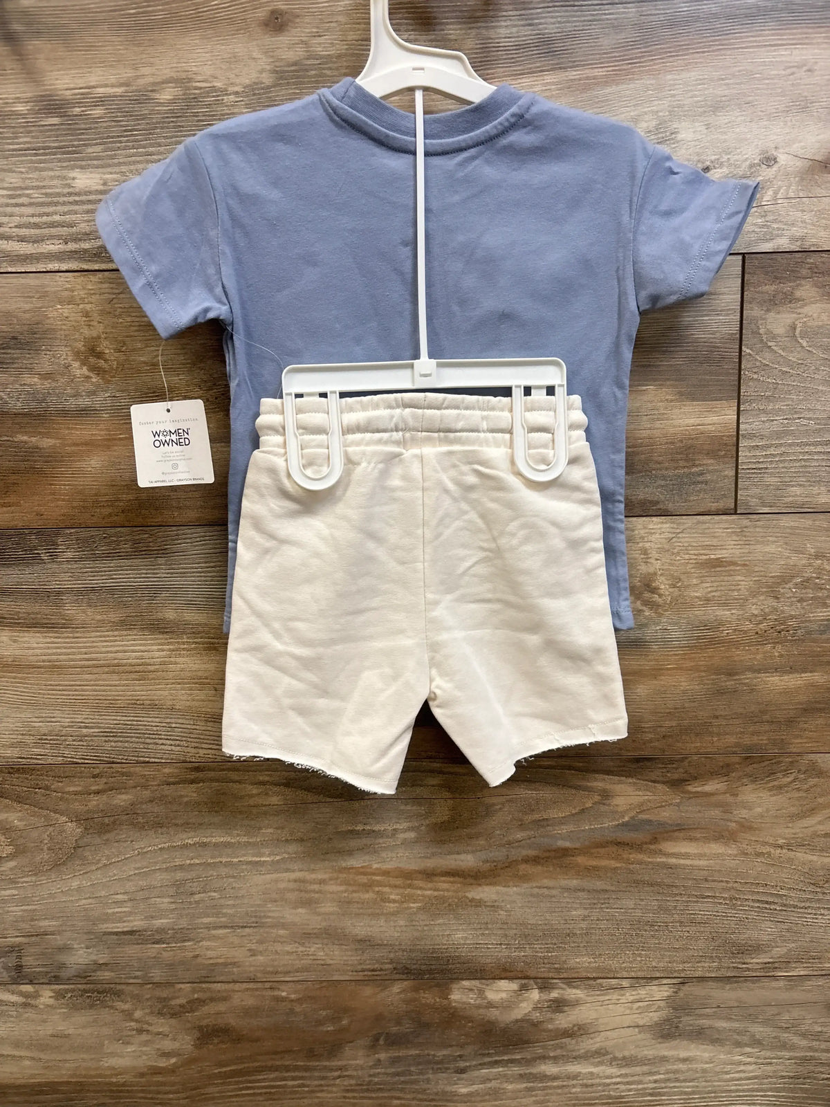 Front view of blue Grayson Mini Surf T-shirt and cream elastic-waist shorts, size 2T, on a hanger against wood