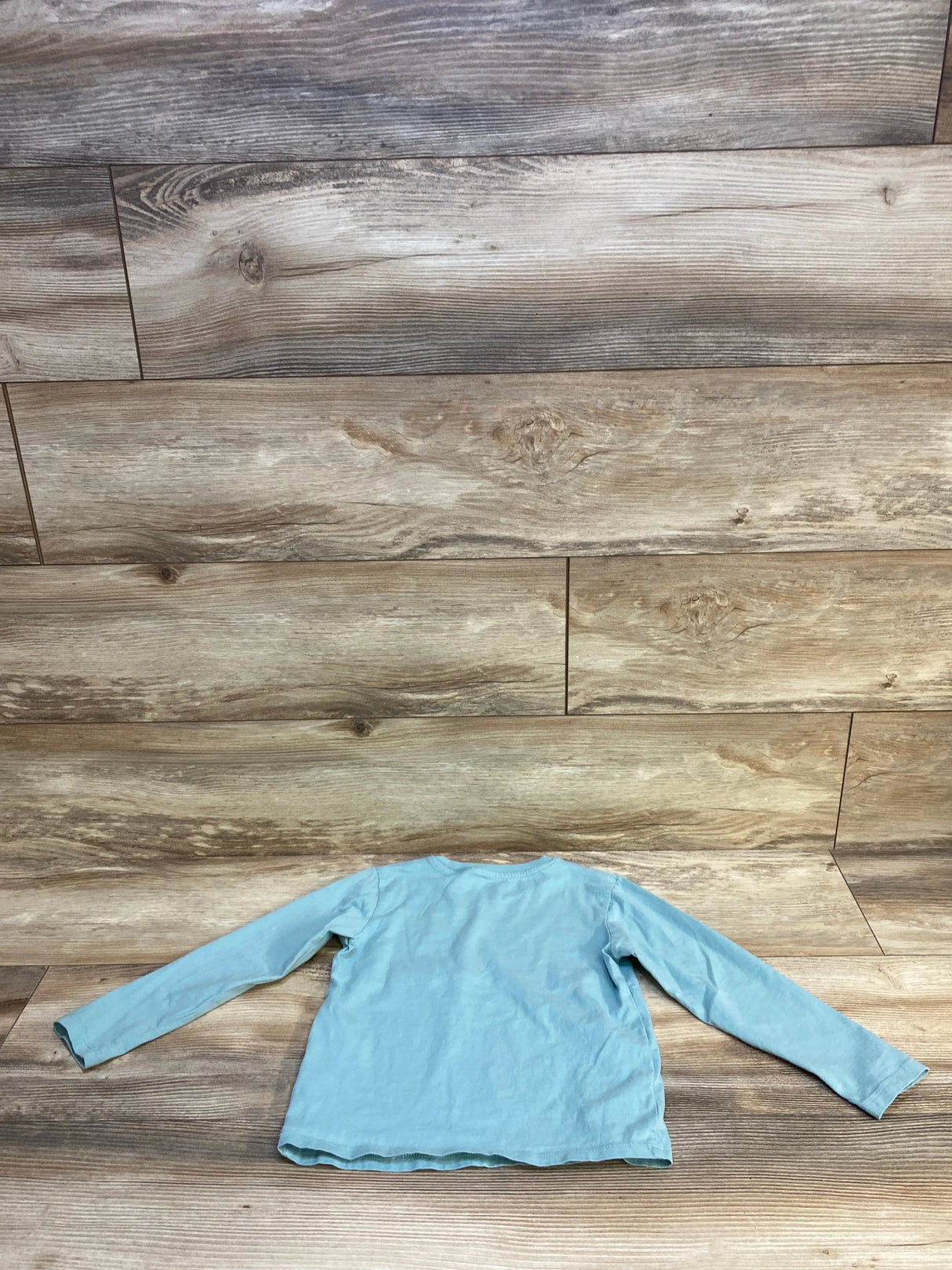 Light blue long sleeve kids shirt, back view, on rustic wood background