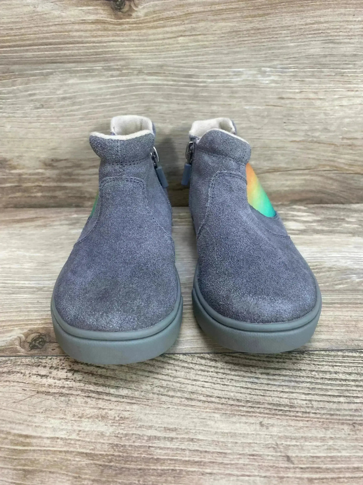 Front view of UGG Hamden II toddler grey suede sneakers showing rounded toes, side zippers and rainbow heart detail on wooden floor background
