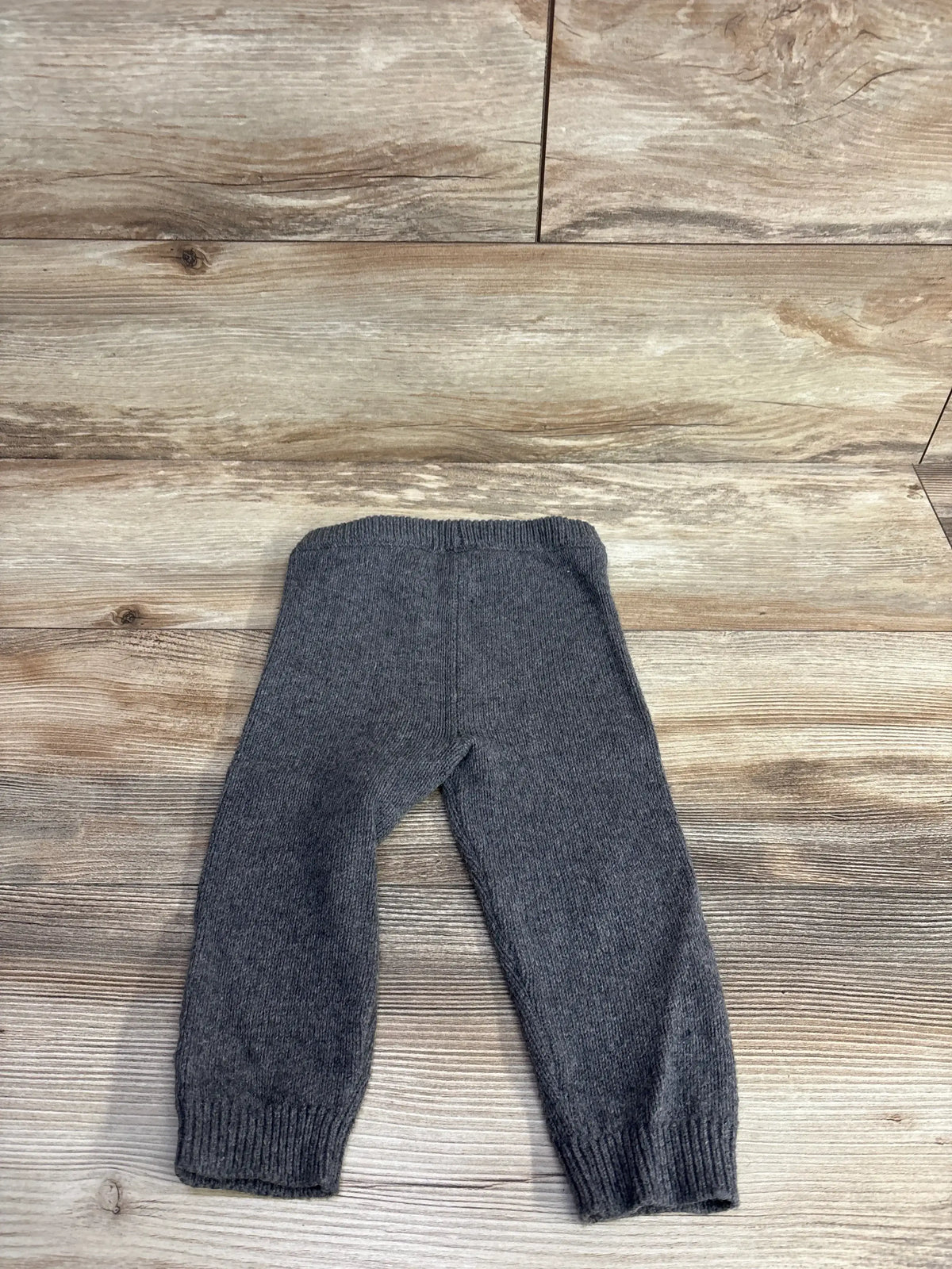 Gray knitted baby pants laid flat on wooden surface, cozy kids clothing from resale store