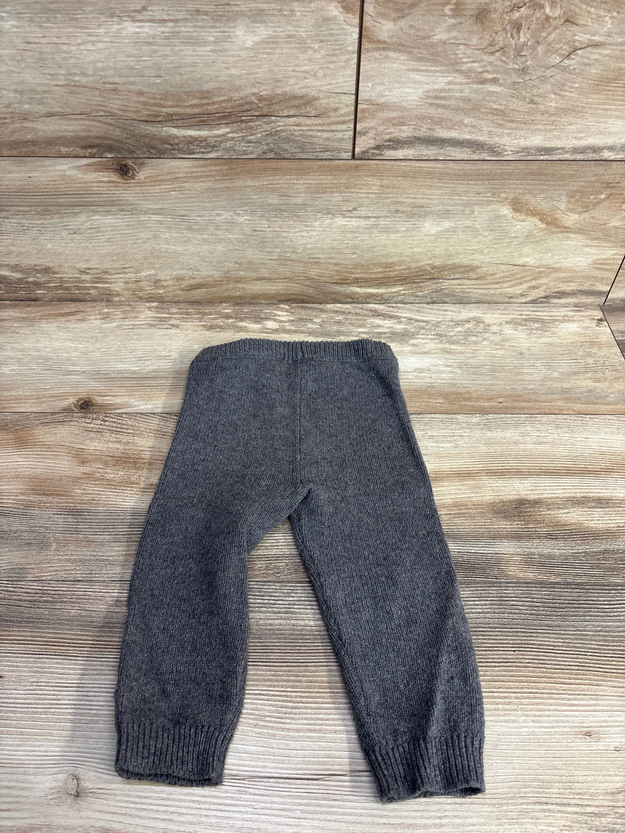 Gray knitted baby pants laid flat on wooden surface, cozy kids clothing from resale store