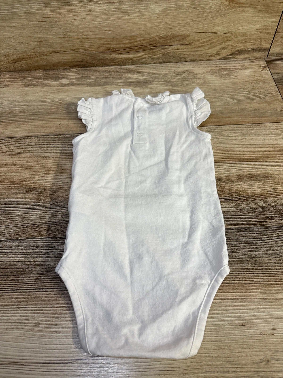 White Du Pareil Au Meme baby bodysuit with ruffle shoulders on a wooden background