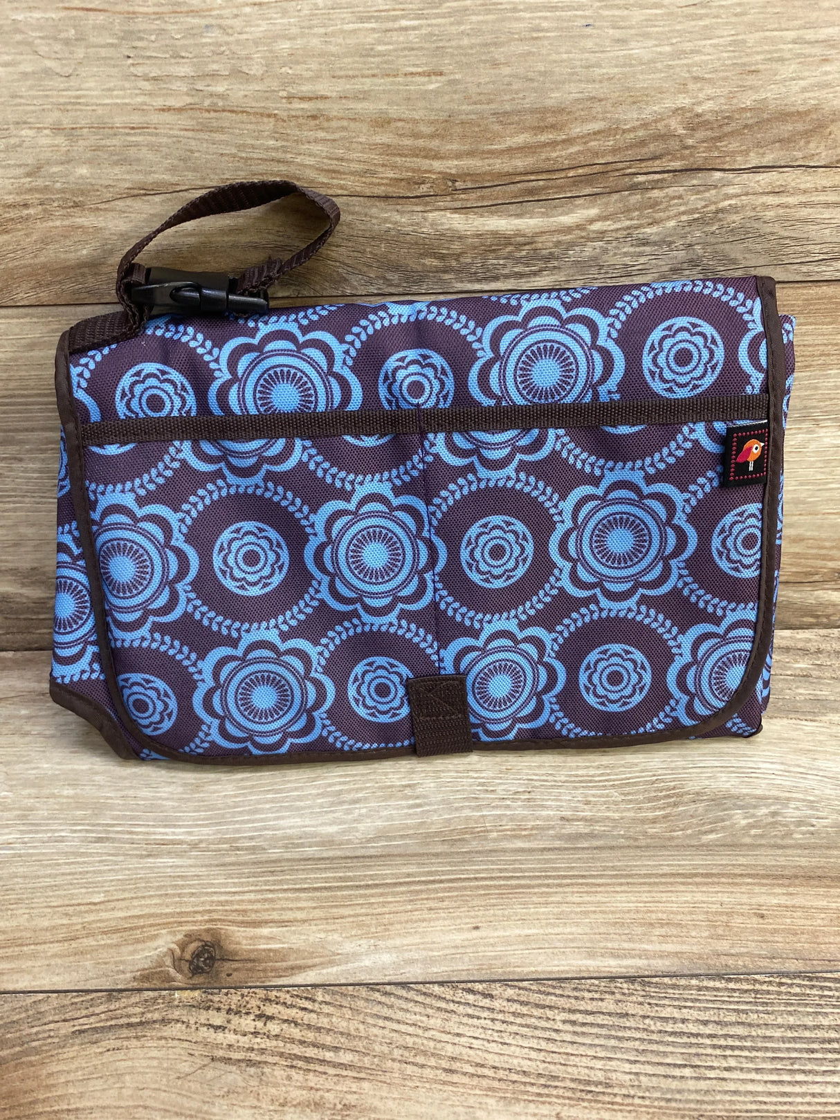 Front view of Avon Tiny Tillia portable changing pad folded showing blue floral circle print, strap attached on wood background