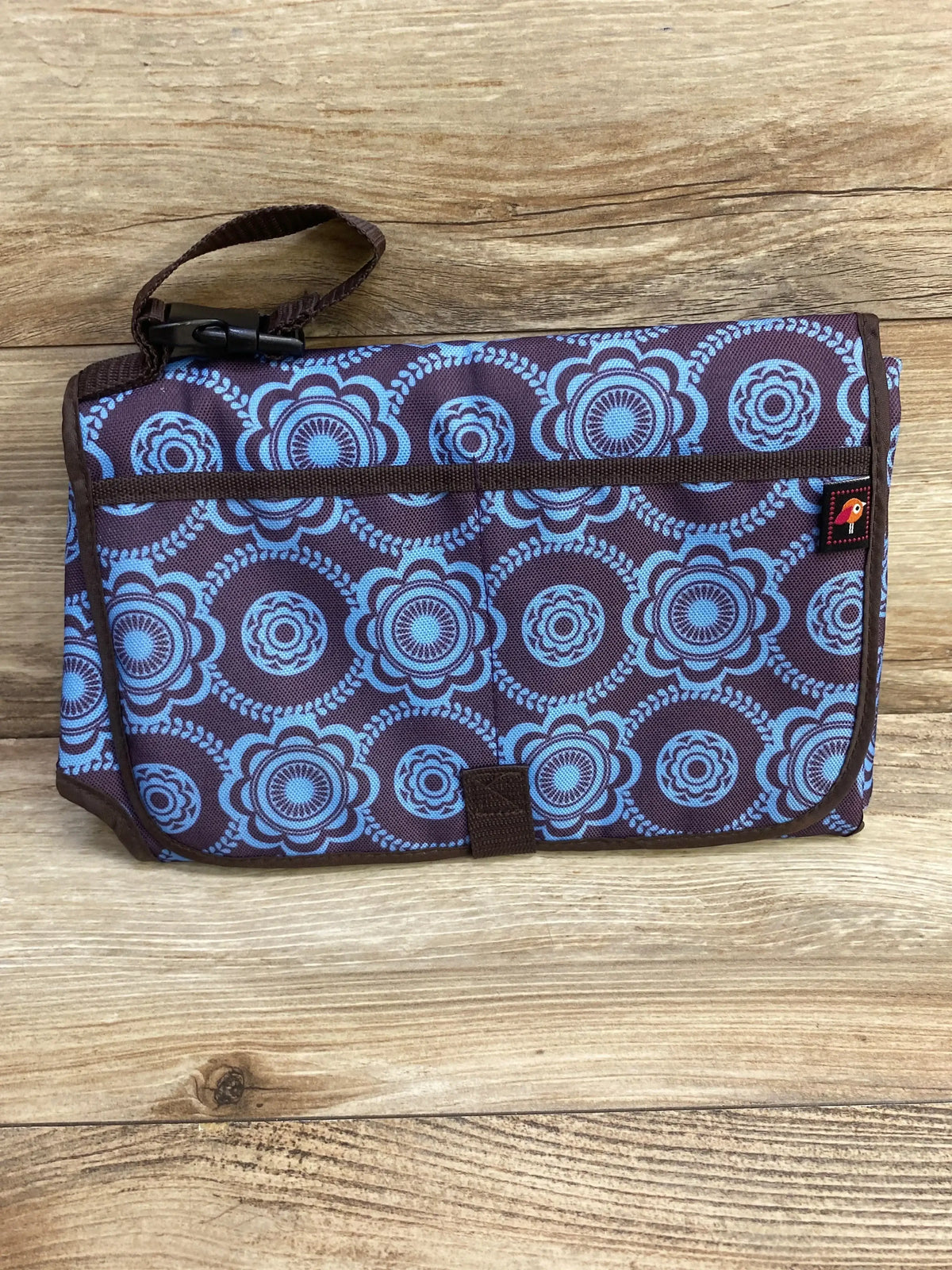 Front view of Avon Tiny Tillia portable changing pad folded showing blue floral circle print, strap attached on wood background