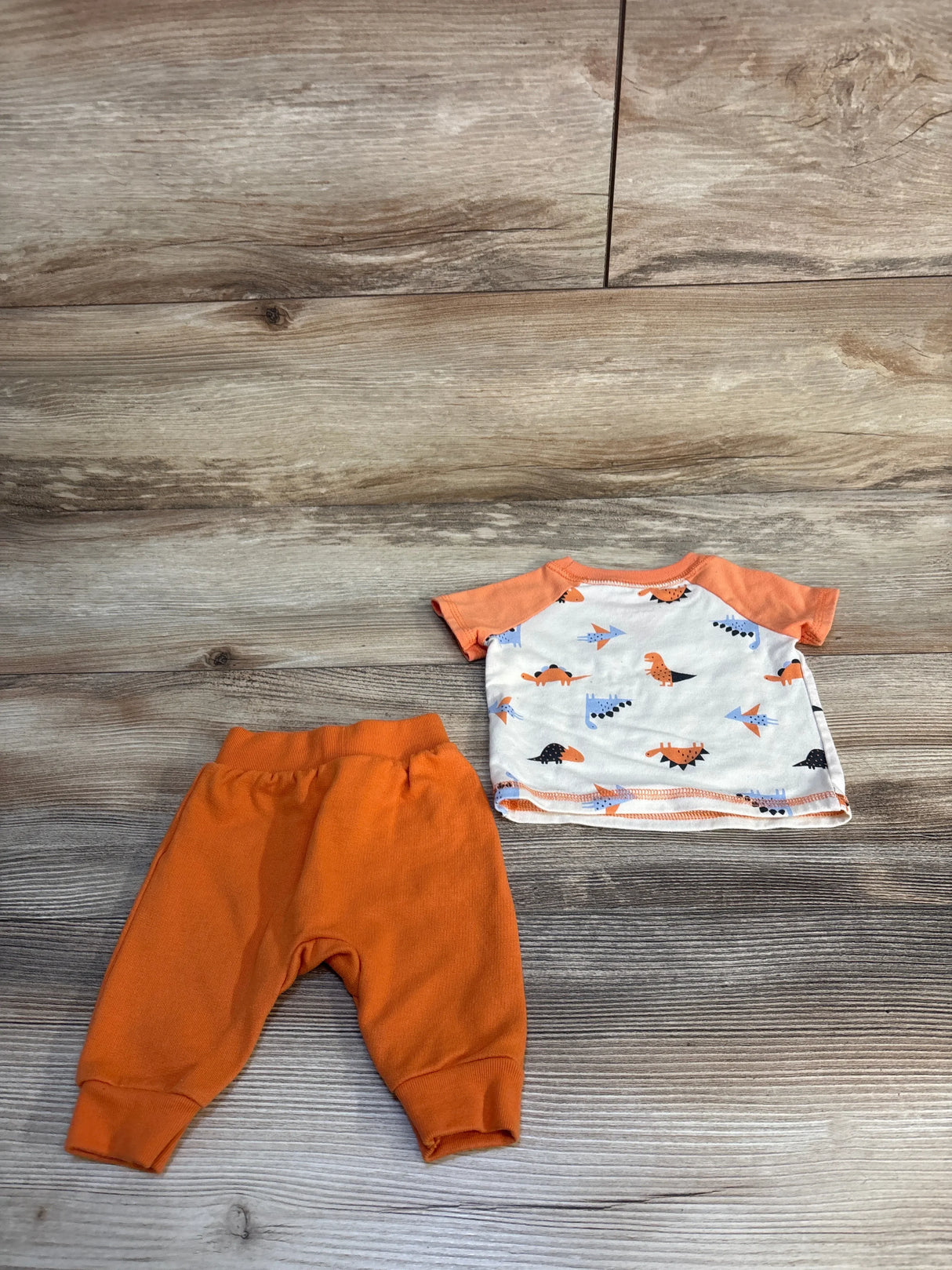 Baby outfit with orange pants and dinosaur print shirt on wood background
