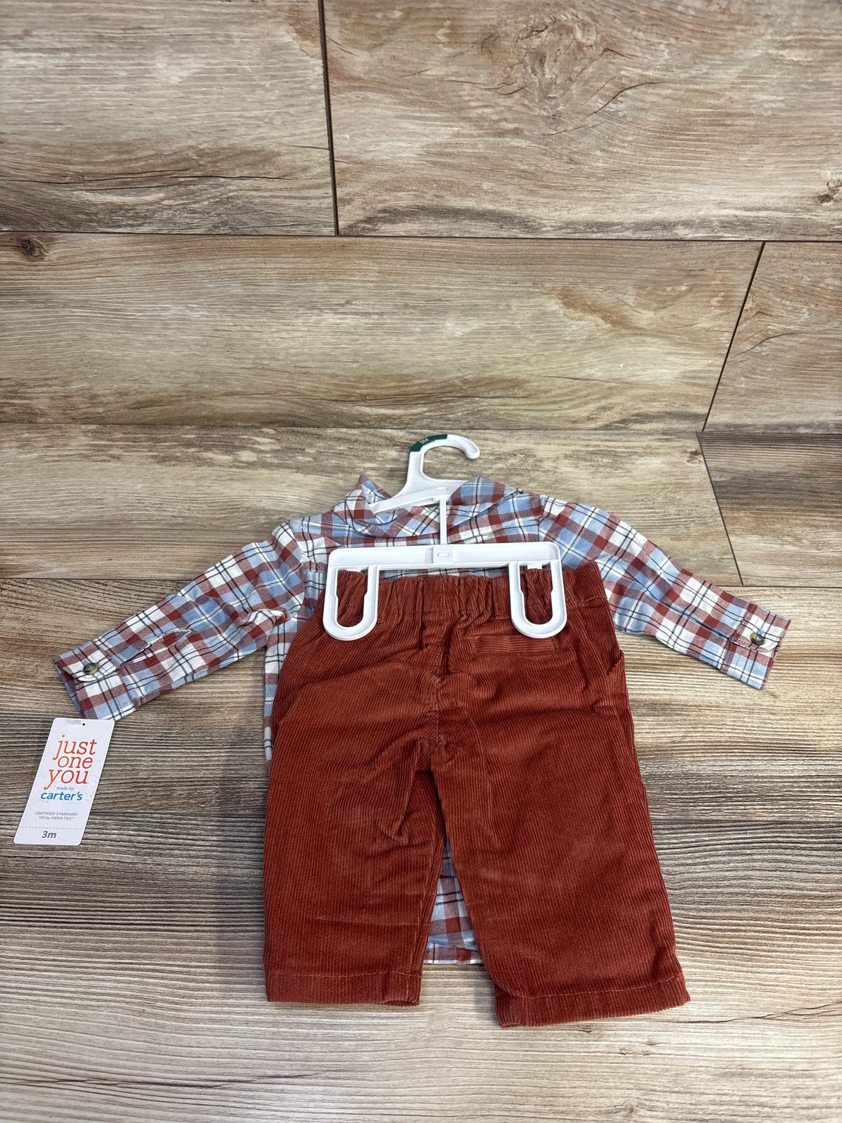 Front view of 2-piece plaid long-sleeve bodysuit and rust corduroy pants set size 3M on a hanger against wood floor