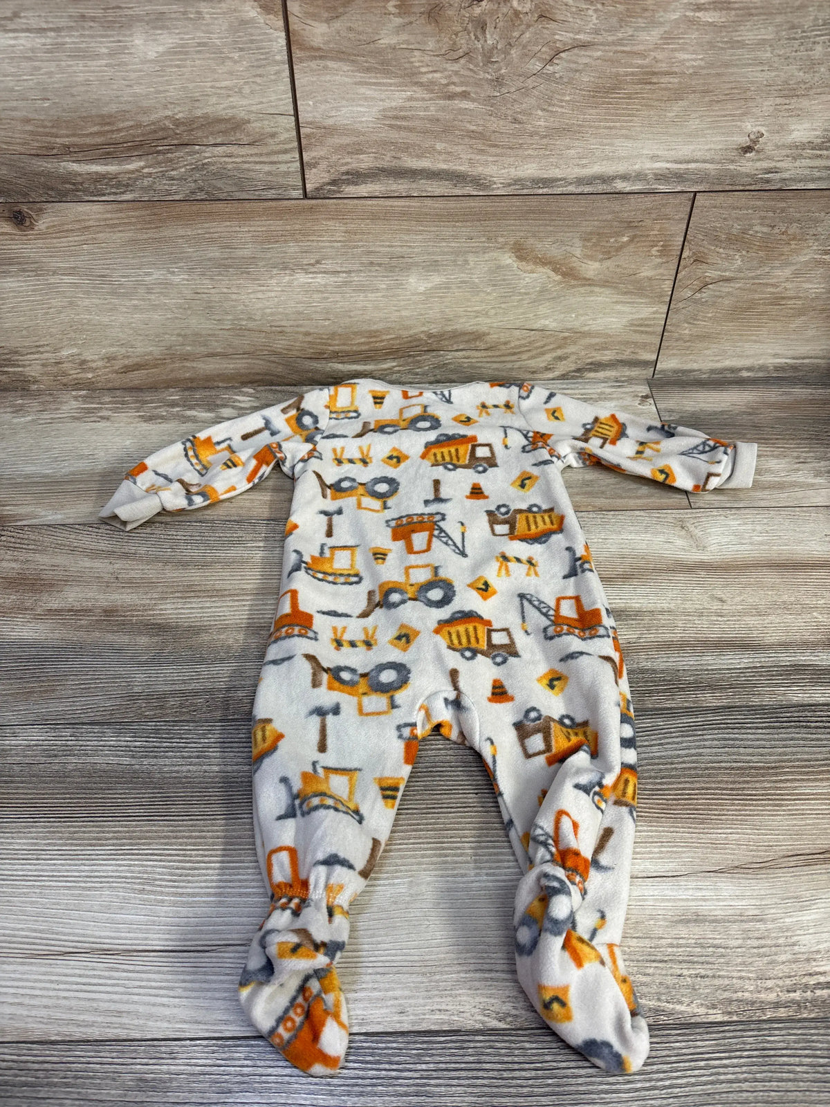 Flat lay of Kids Headquarters construction sleeper in tan, size 6 months, with construction vehicle print on wood flooring