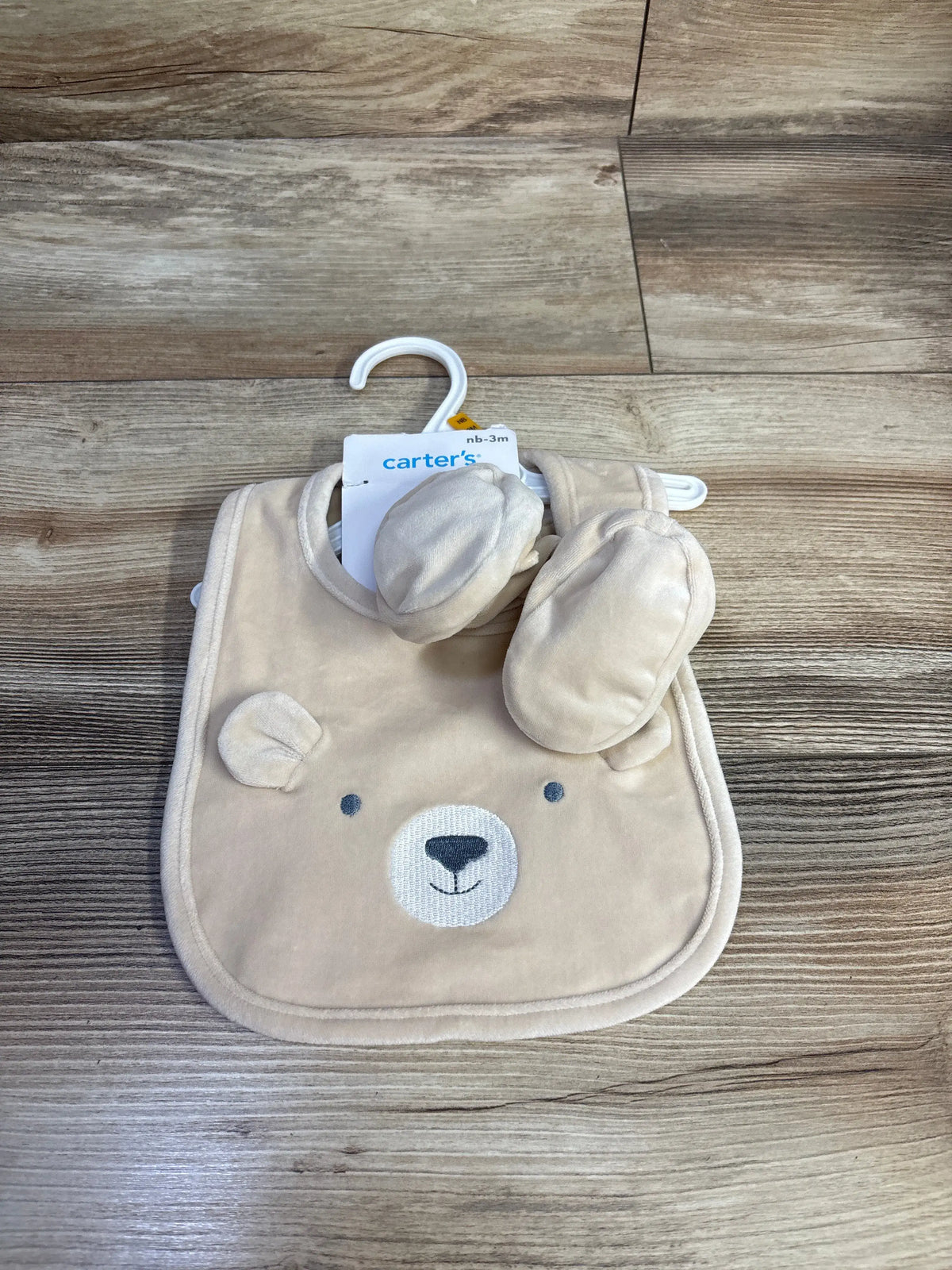 Front view of Carters beige two piece bib and booties set showcasing bear face bib and matching booties on a wood grain floor