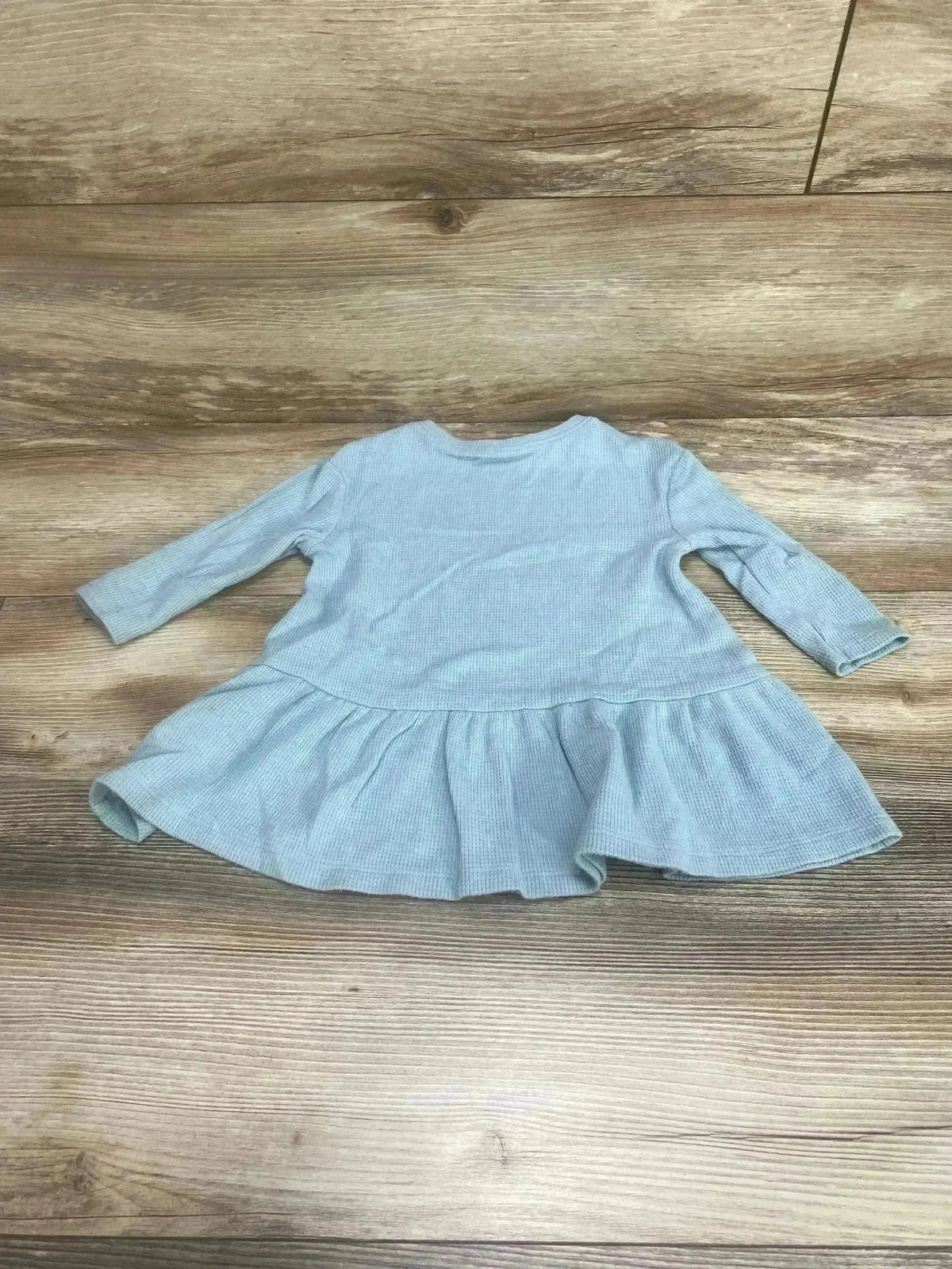 Flat lay of blue Old Navy peplum thermal shirt (12-18 months) showcasing long sleeves and ruffled peplum with wood floor background