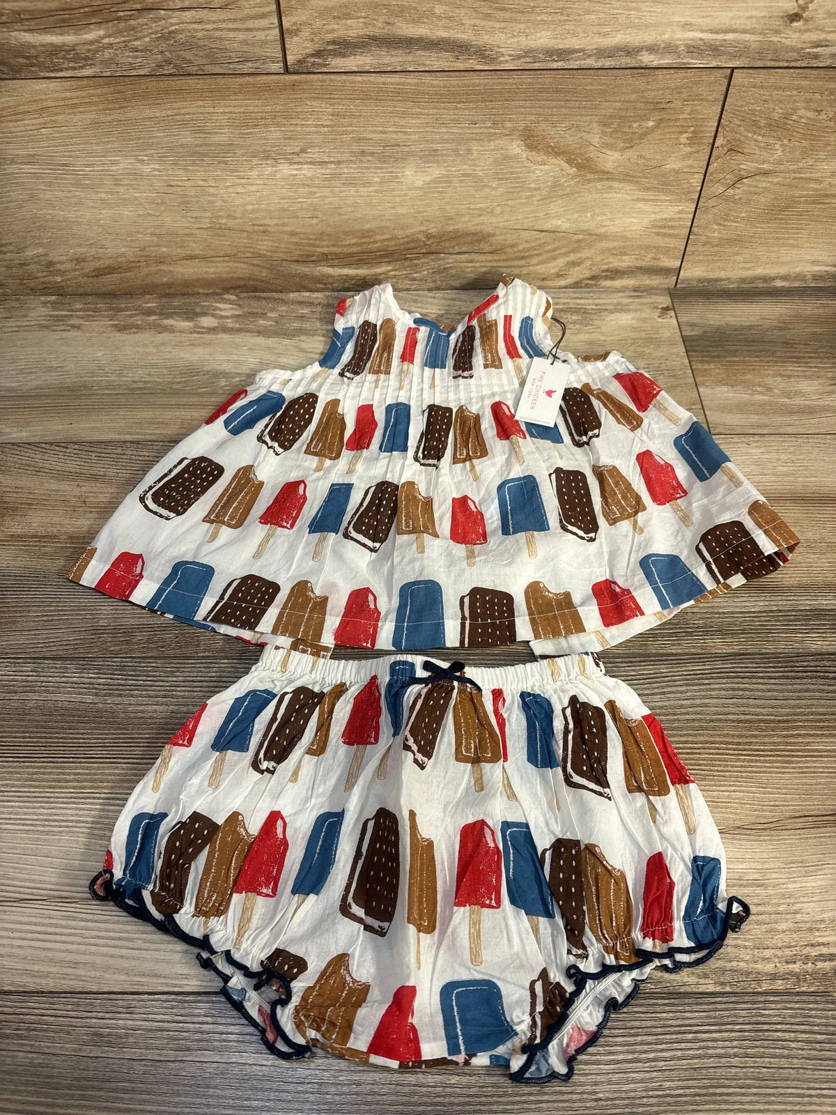 Top-down view of Pink Chicken baby girls Jaipur set in Popsicles, showing pintucked A-line top and bloomers on wood flooring