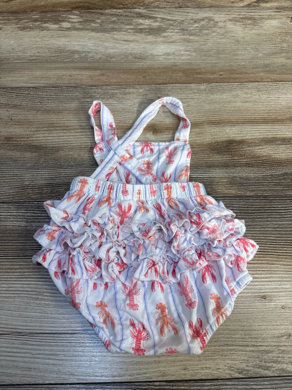 Baby ruffle romper with pink lobster print and crossed straps on wooden background
