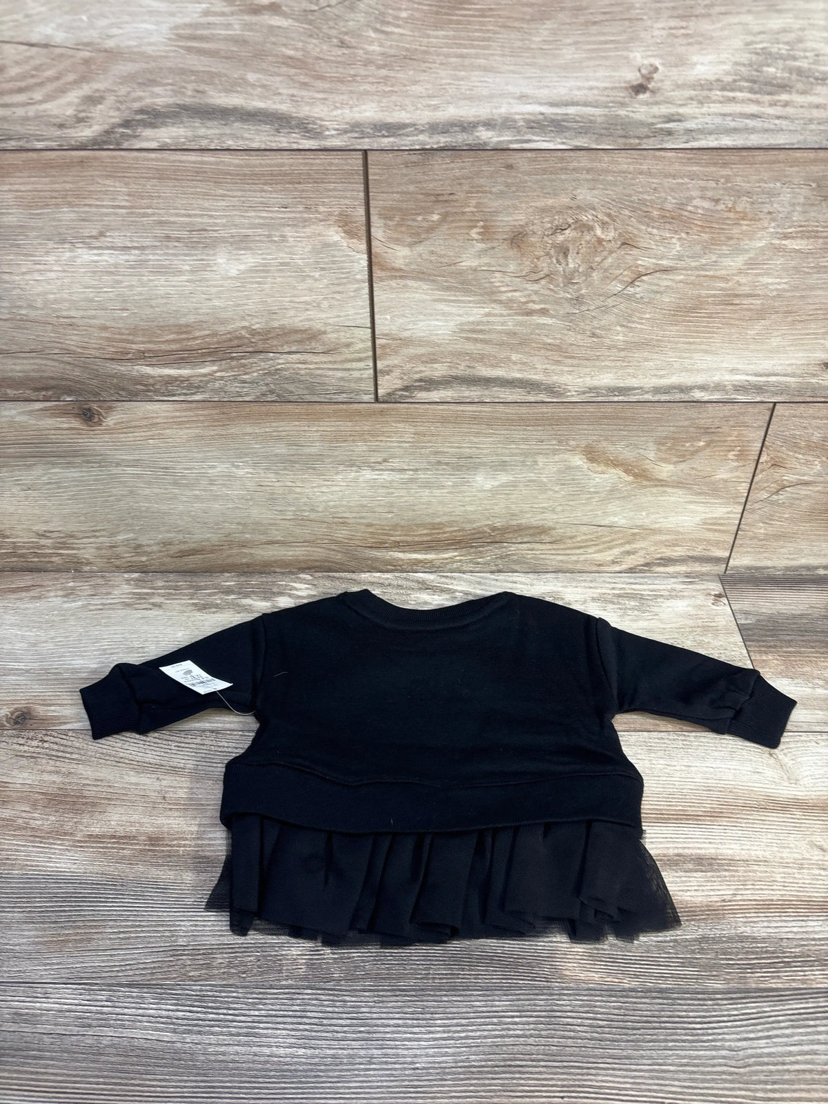 Top view of Baby Gap VintageSoft black sweatshirt showcasing long sleeves and tulle hem on a wood floor