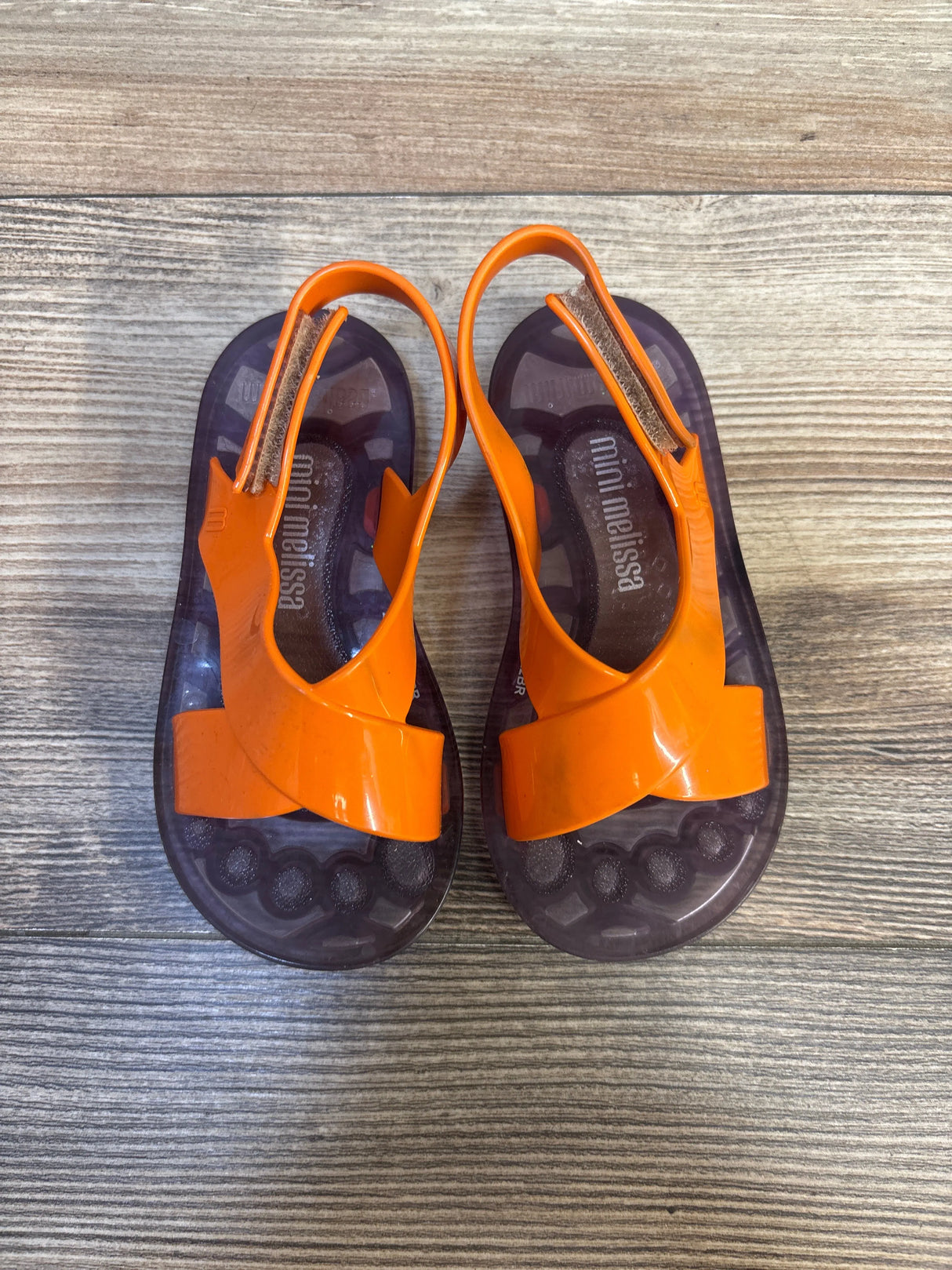 Pair of orange Mini Melissa toddler sandals on wood floor, kids summer footwear