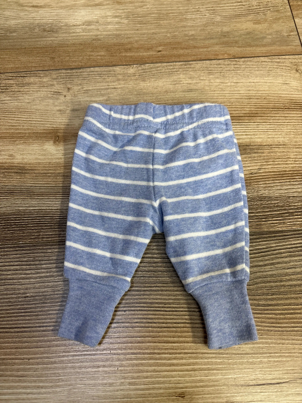 Front view of Child of Mine preemie pants showcasing blue and white horizontal stripes on a wood surface