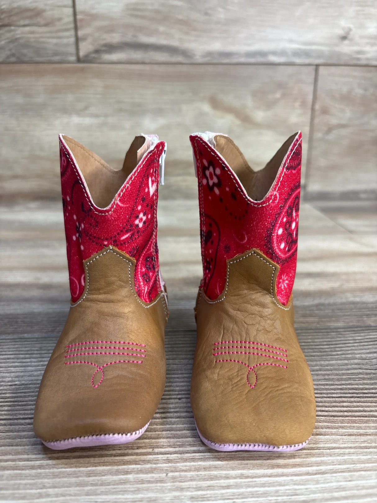 Pair of toddler brown cowboy boots with red paisley tops on wood floor